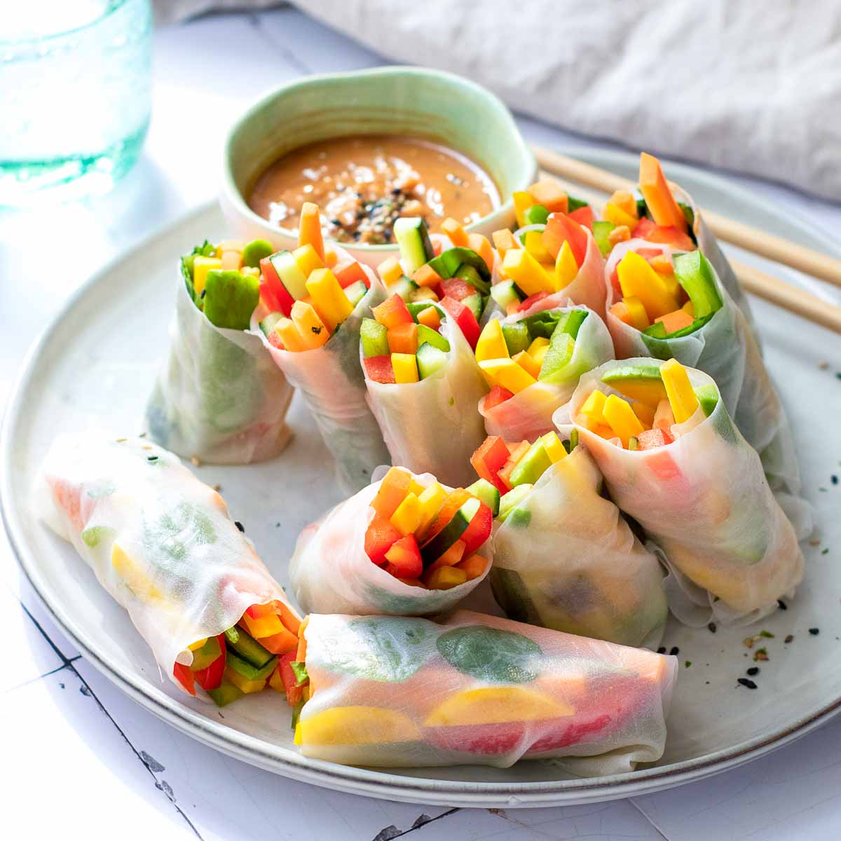 Side view of rainbow veggies rice paper rolls with hoisin sauce in the background.