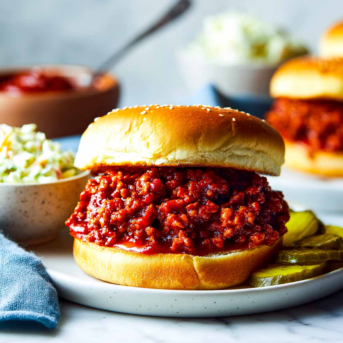Vegan sloppy joe sandwich on a bun with coleslaw and pickles on the side.