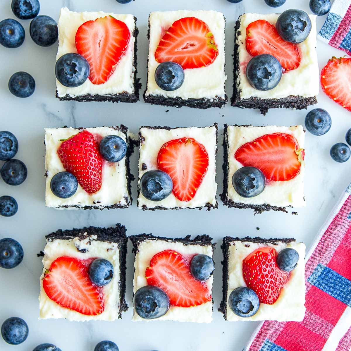Top view of Oreo cheesecake bars topped with fresh strawberries and blueberries on marble surface.
