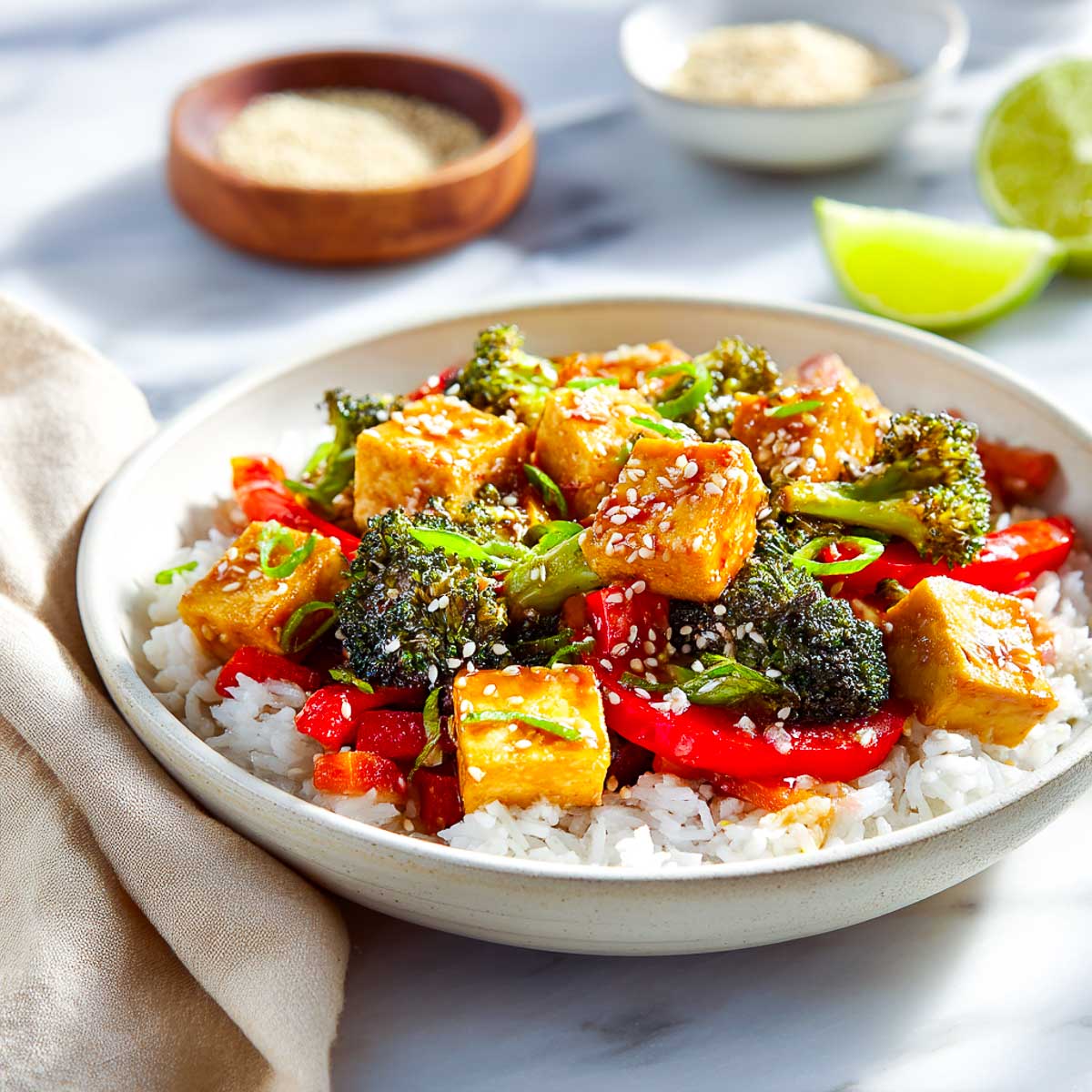 Tofu stir-fry with broccoli and red pepper over rice in a ceramic bowl.