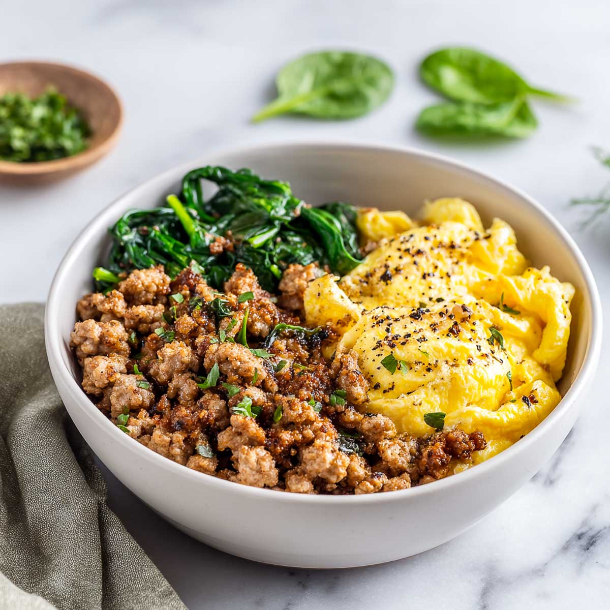 Breakfast bowl with turkey sausage, scrambled eggs, and spinach on marble.