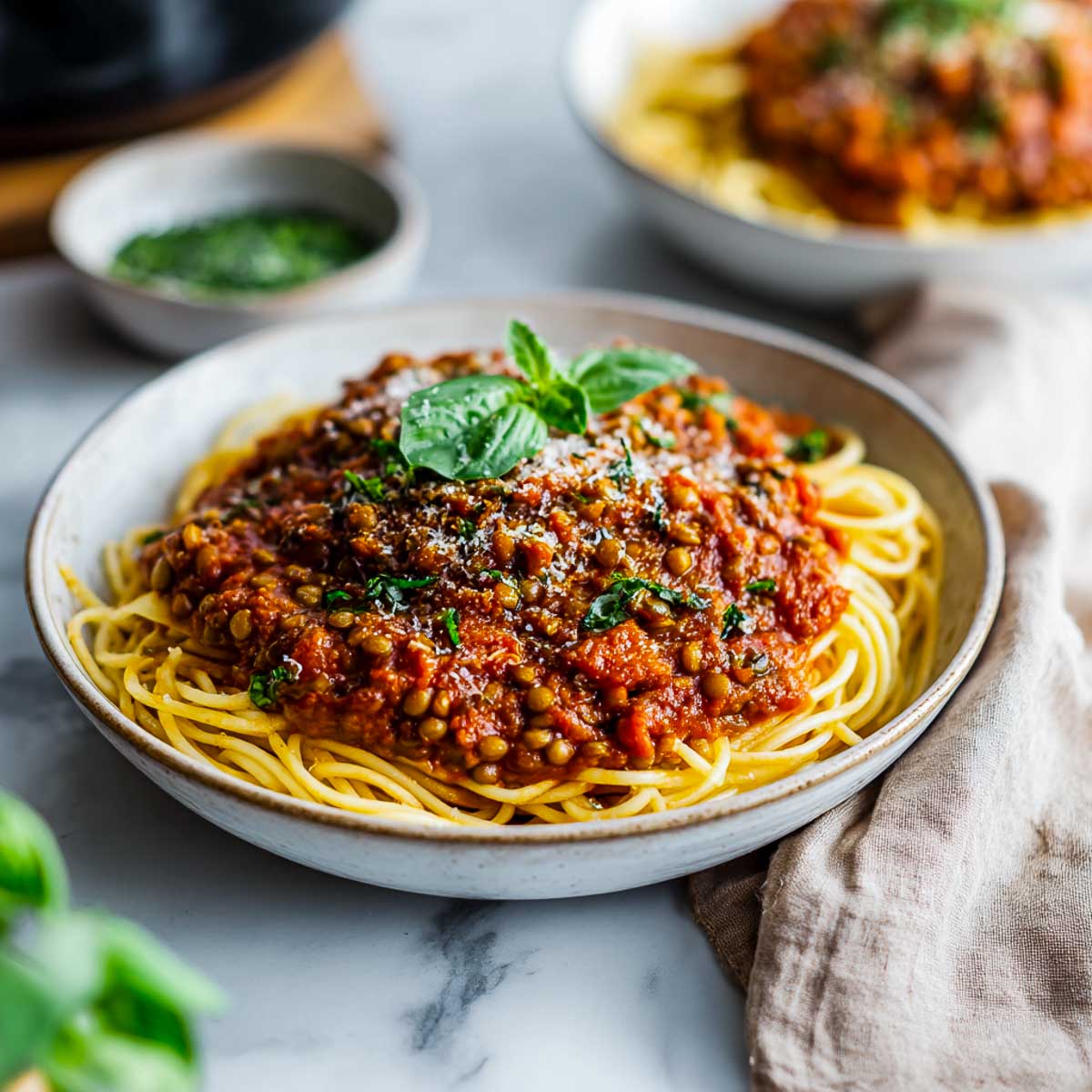Vegan bolognese served over spaghetti in a ceramic bowl, topped with basil.