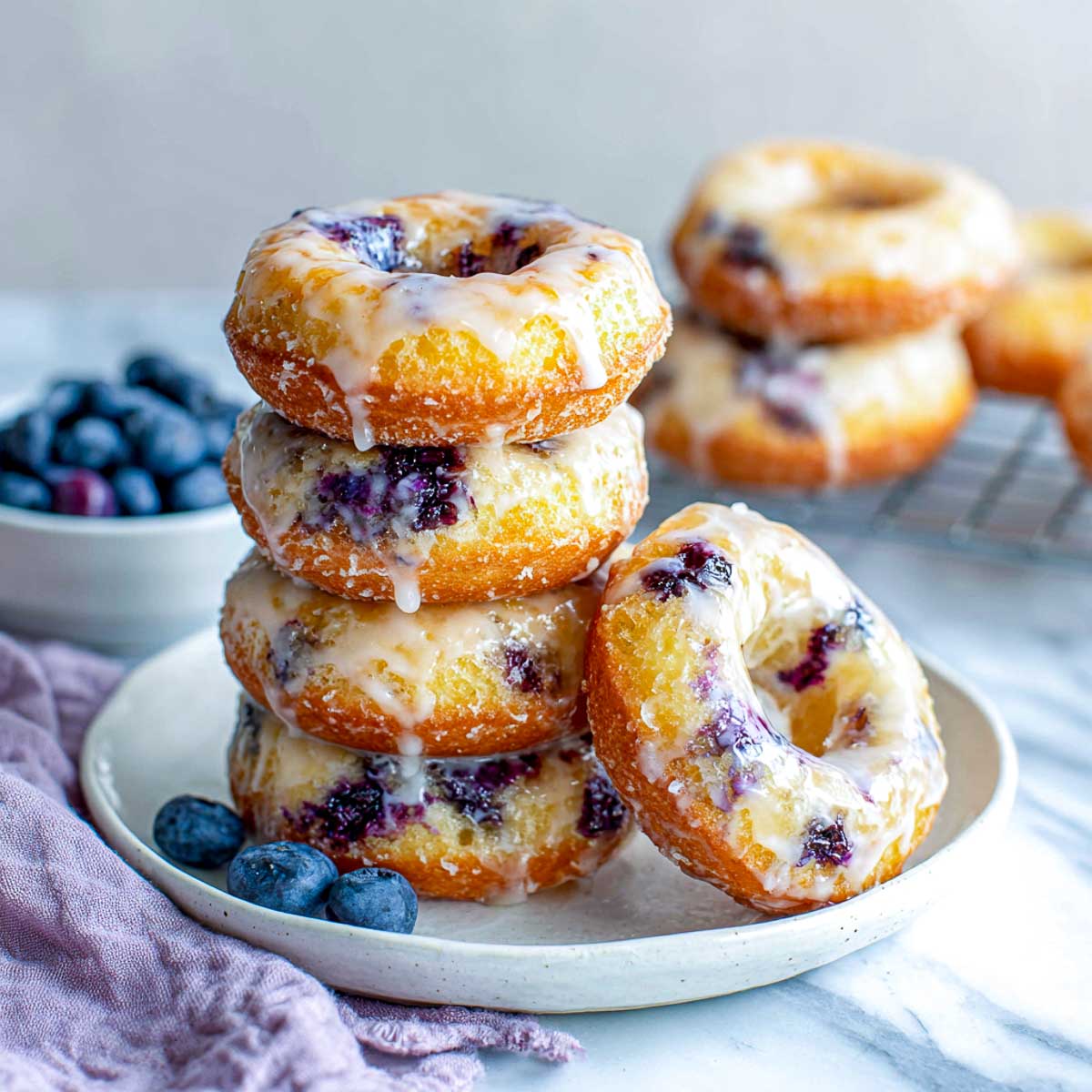 Slightly angled view of glazed blueberry donuts stacked on a plate with fresh berries.