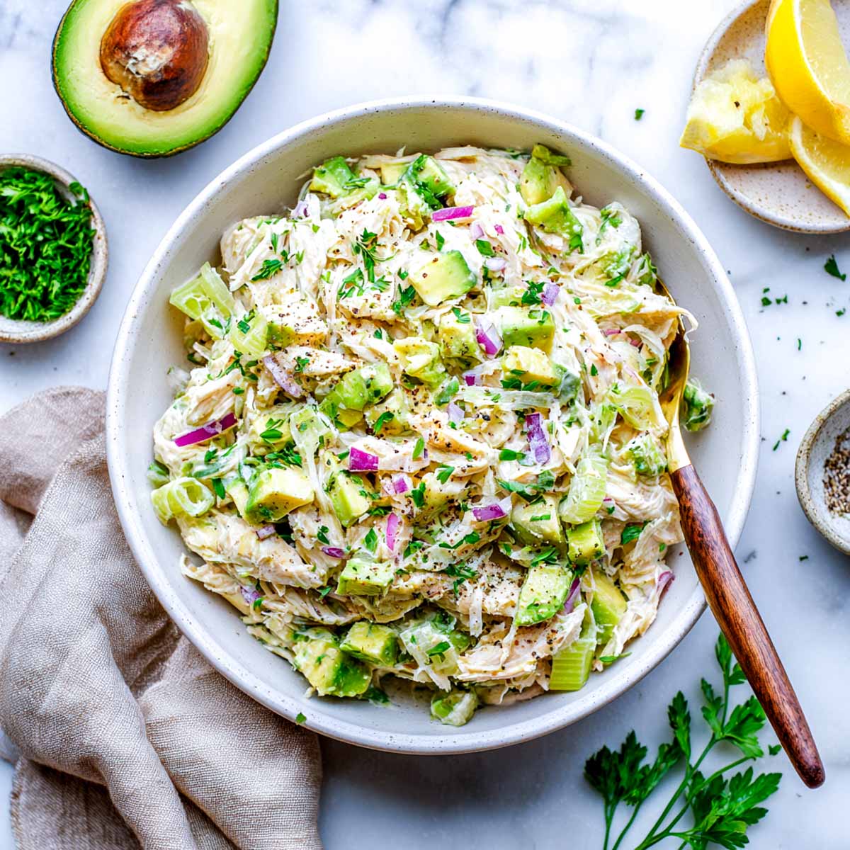 Shredded chicken salad with avocado, red onion, and celery in a white bowl.
