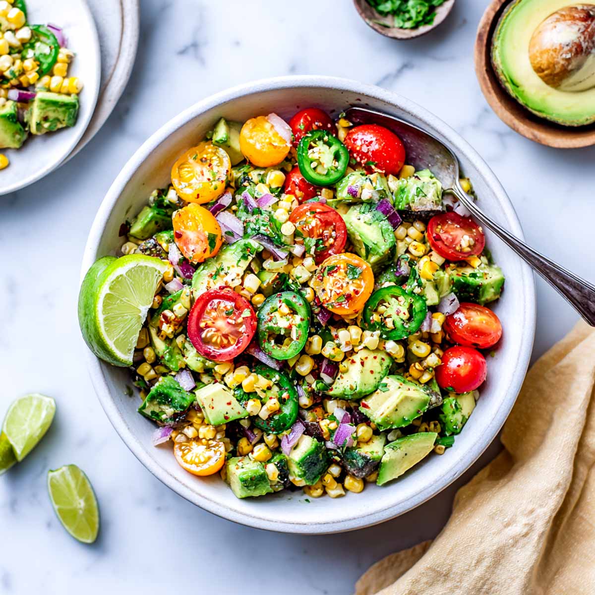 Avocado corn salad with tomatoes, red onion, jalapeños, and lime wedges.