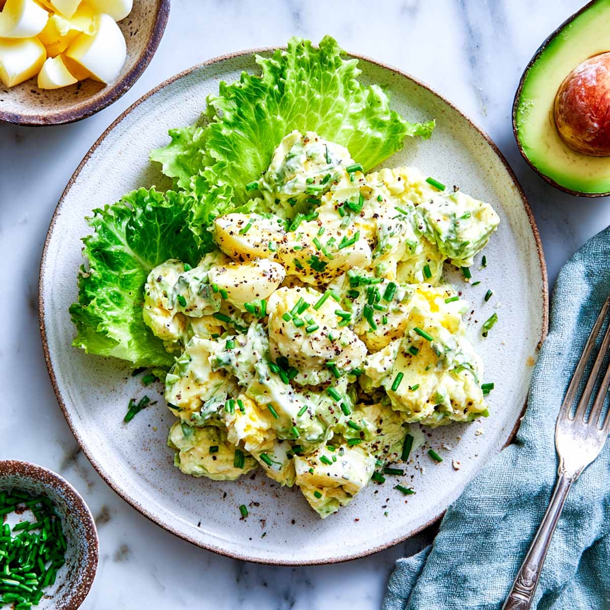 Creamy avocado egg salad served on lettuce with chives and black pepper.