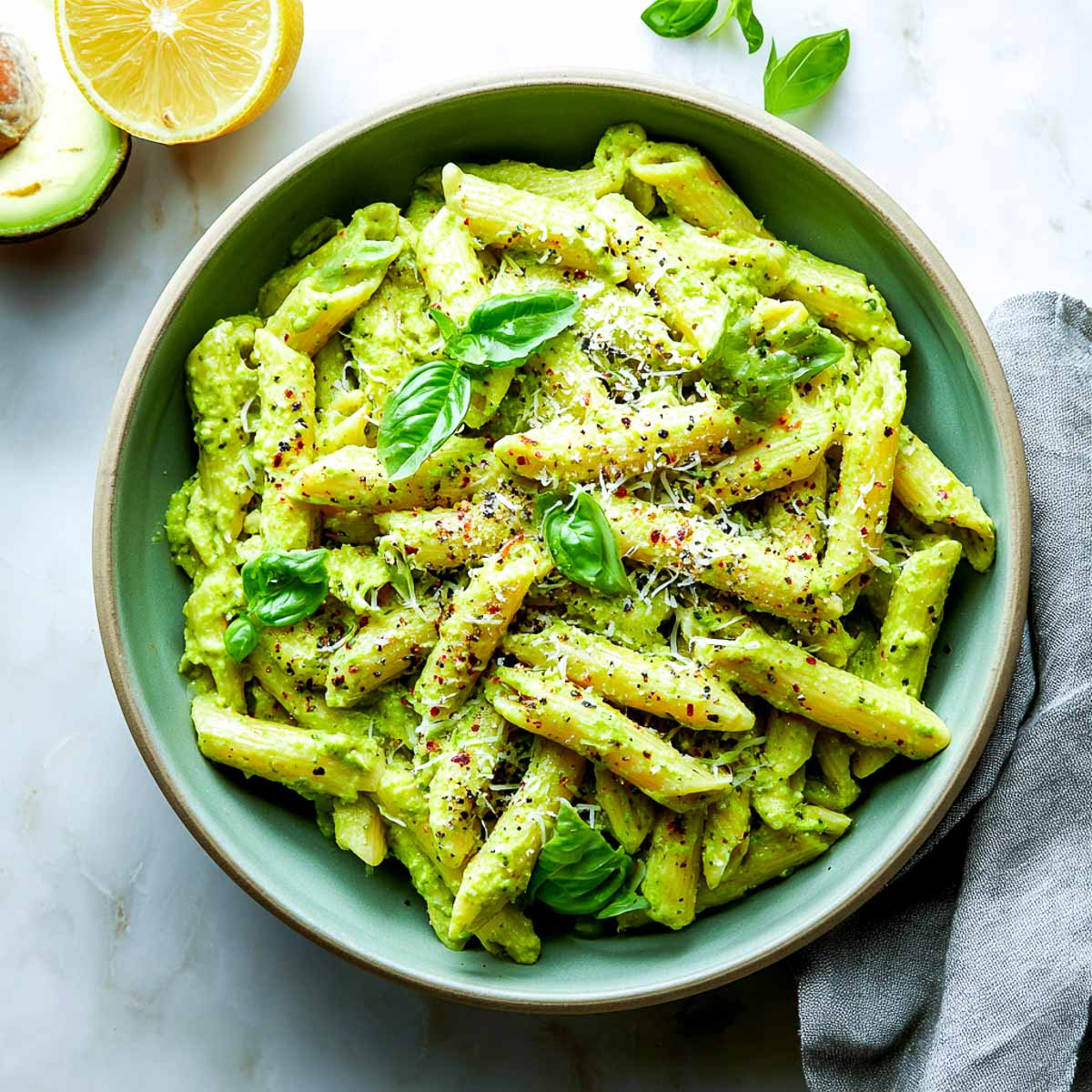 Penne pasta coated in creamy avocado pesto sauce with basil and cheese.