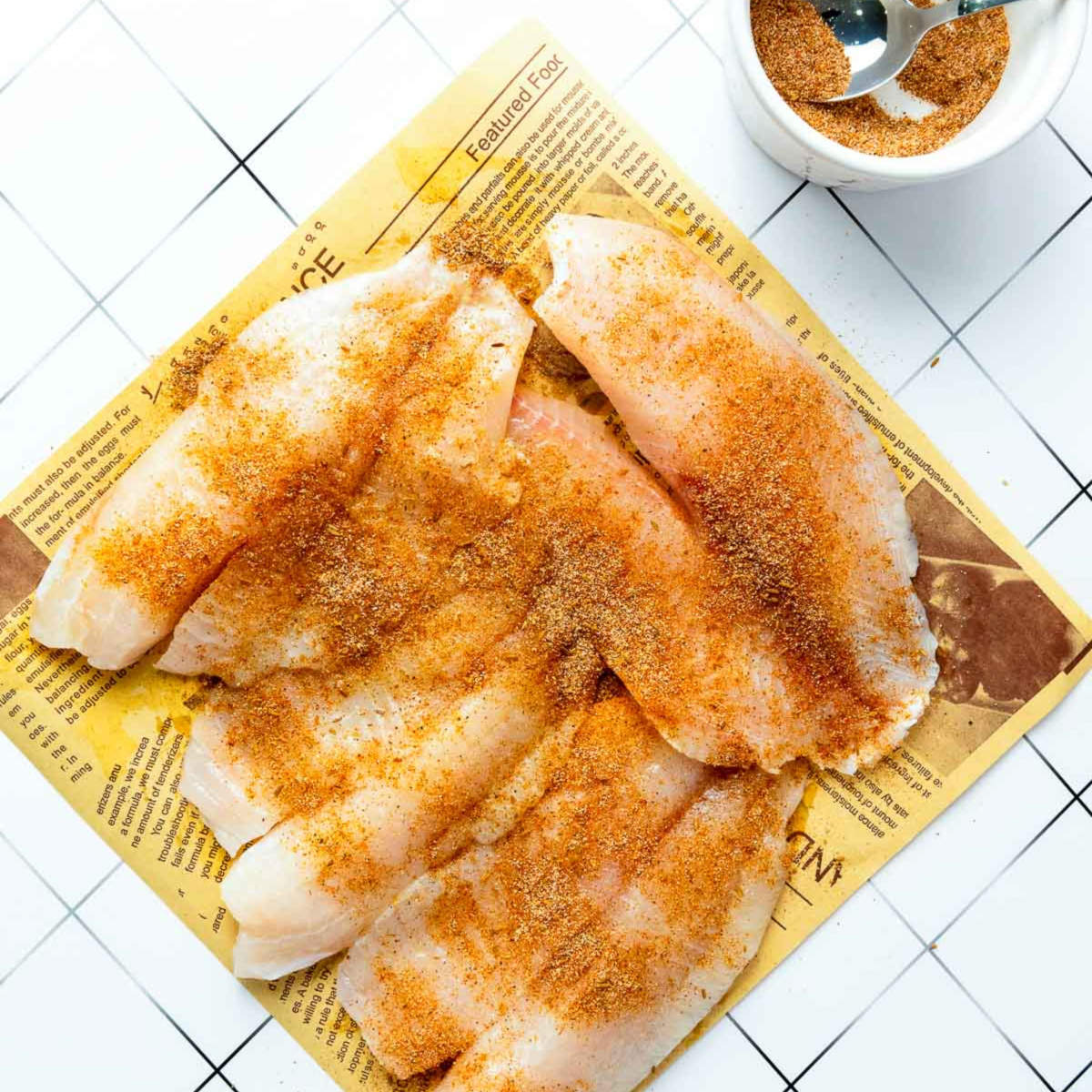 Raw tilapia fillets on a tray coated with homemade blackening spice blend, ready for cooking.