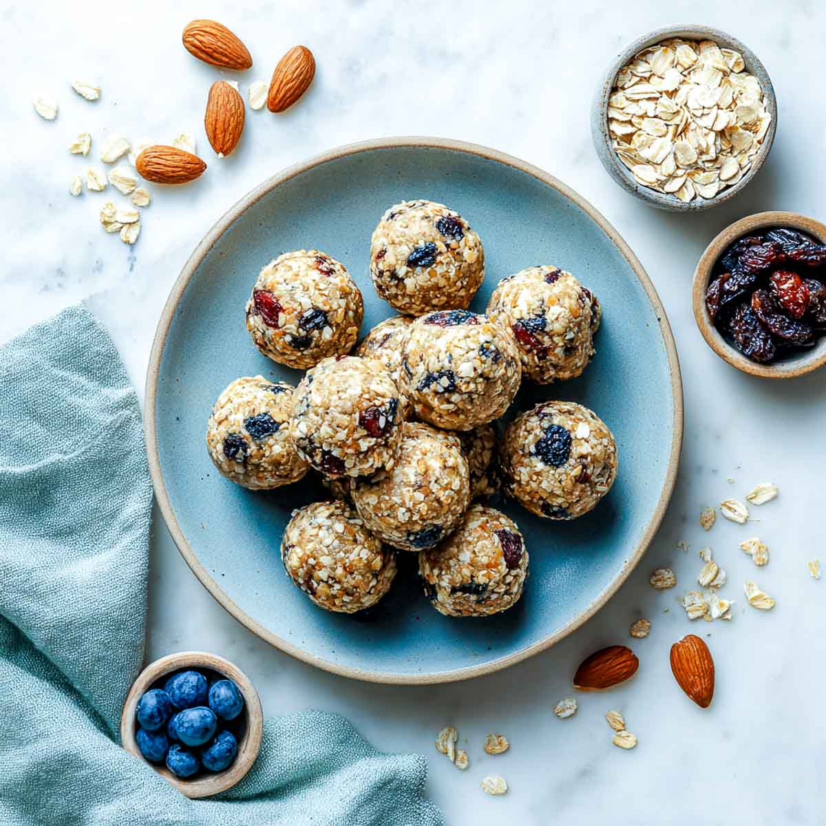 Top-down view of blueberry almond energy balls on a sage plate with oats and berries.