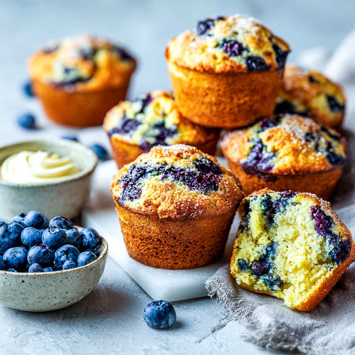 Slightly angled view of blueberry cornbread muffins with one split open on marble.