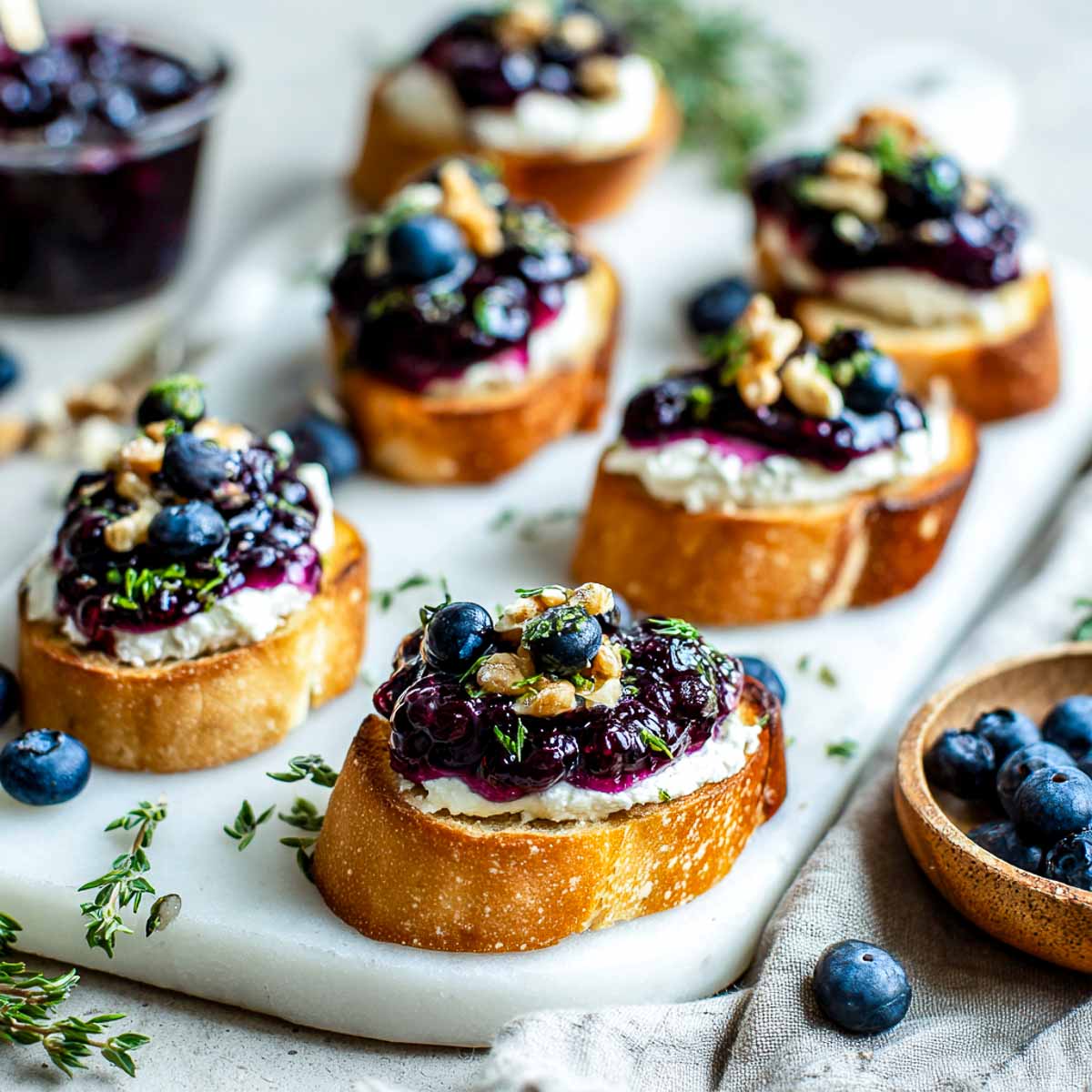Slightly angled view of blueberry goat cheese crostini topped with thyme and walnuts.