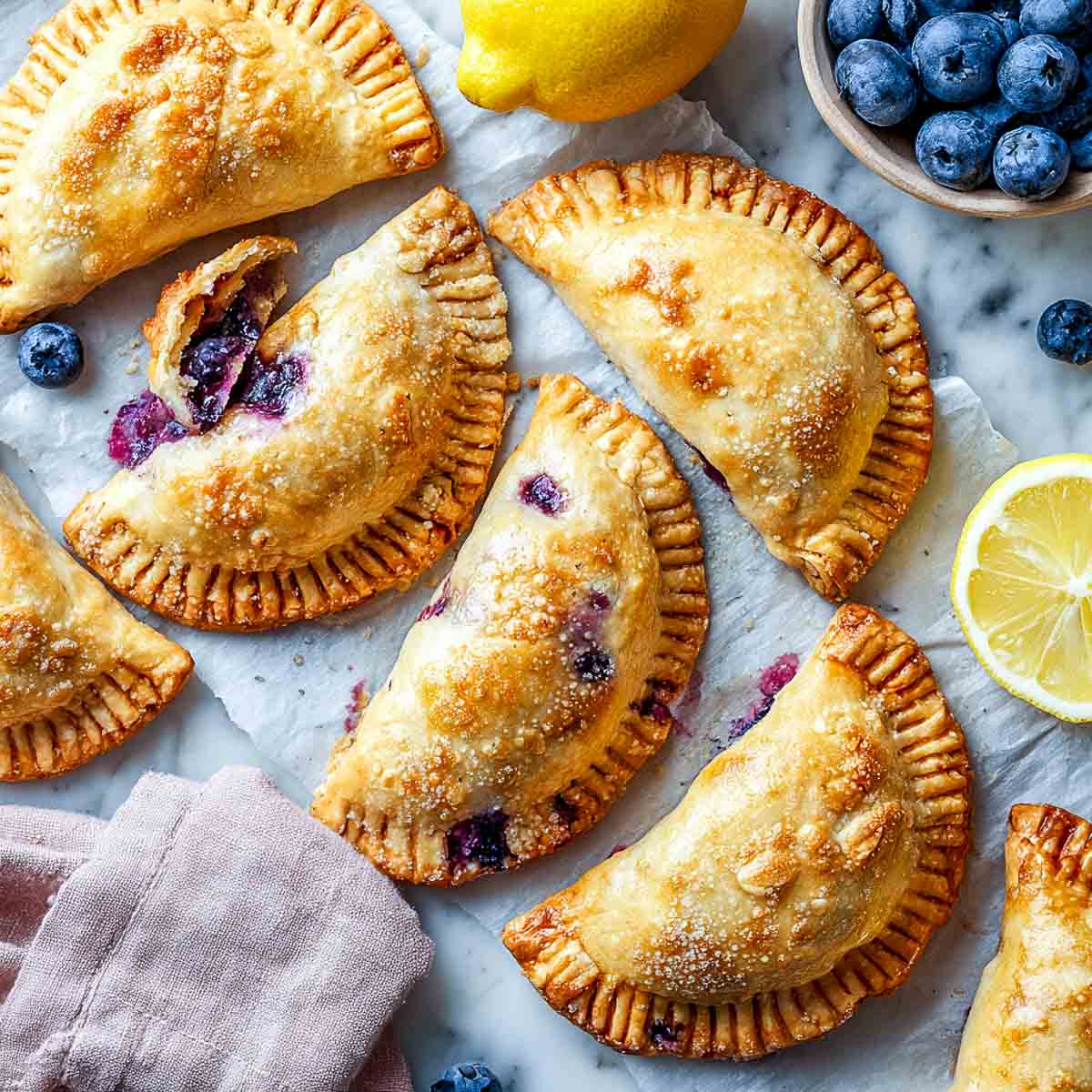 Top-down view of blueberry hand pies with golden crusts and bubbling fruit on parchment.