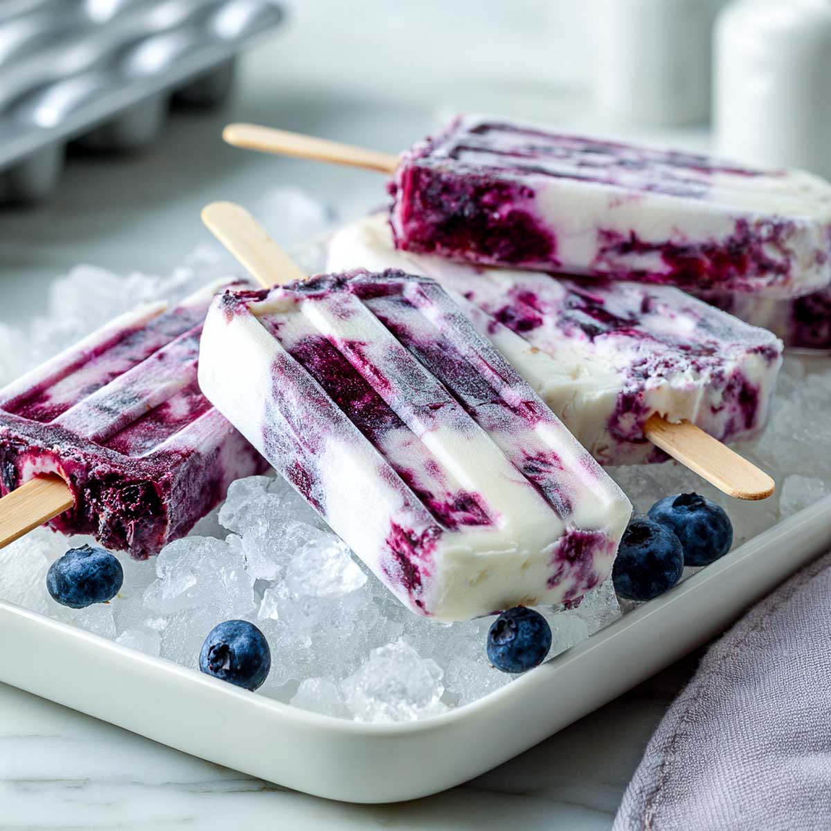 Slightly angled view of blueberry yogurt popsicles resting on crushed ice with fresh berries.