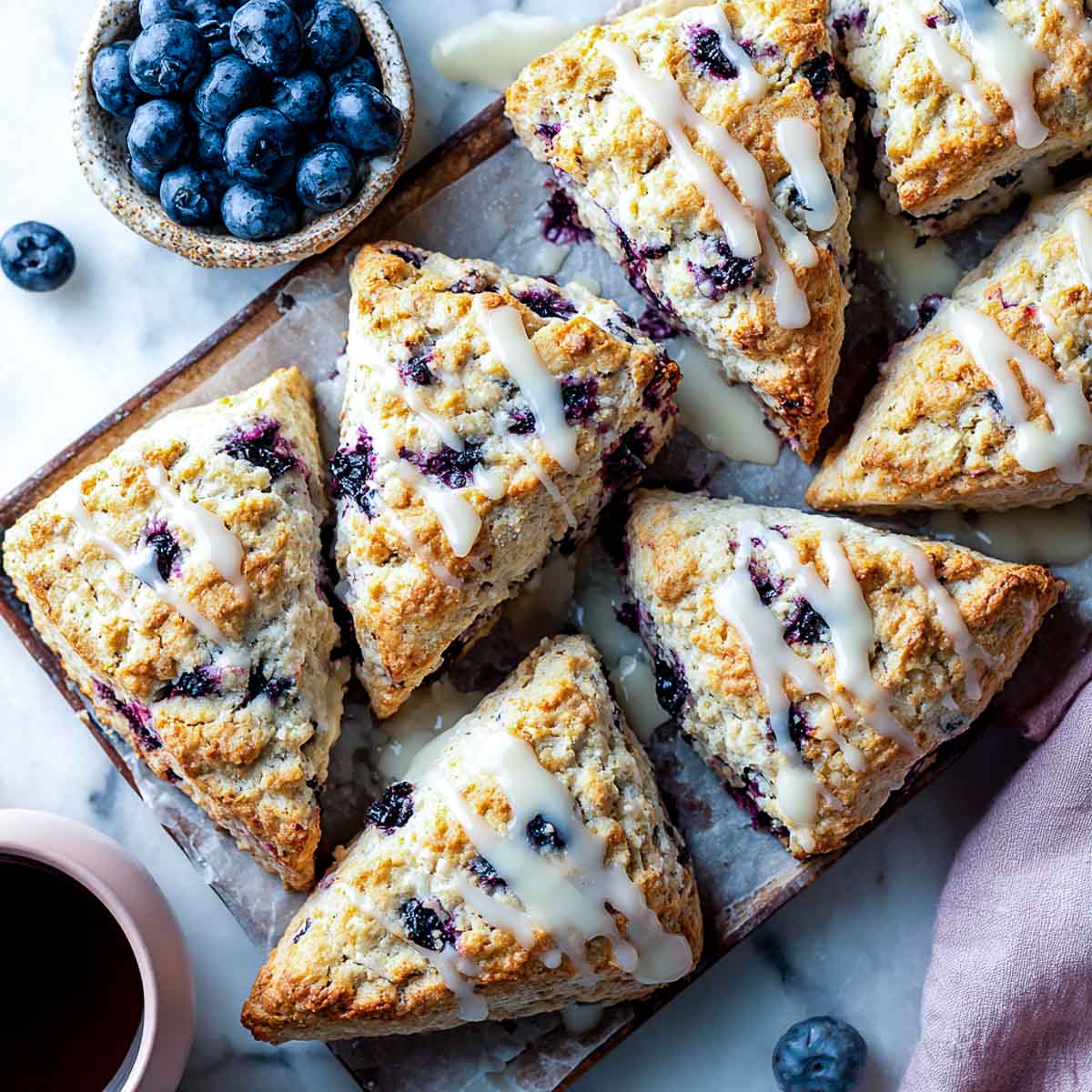 Top-down view of blueberry scones with vanilla glaze on parchment and marble.