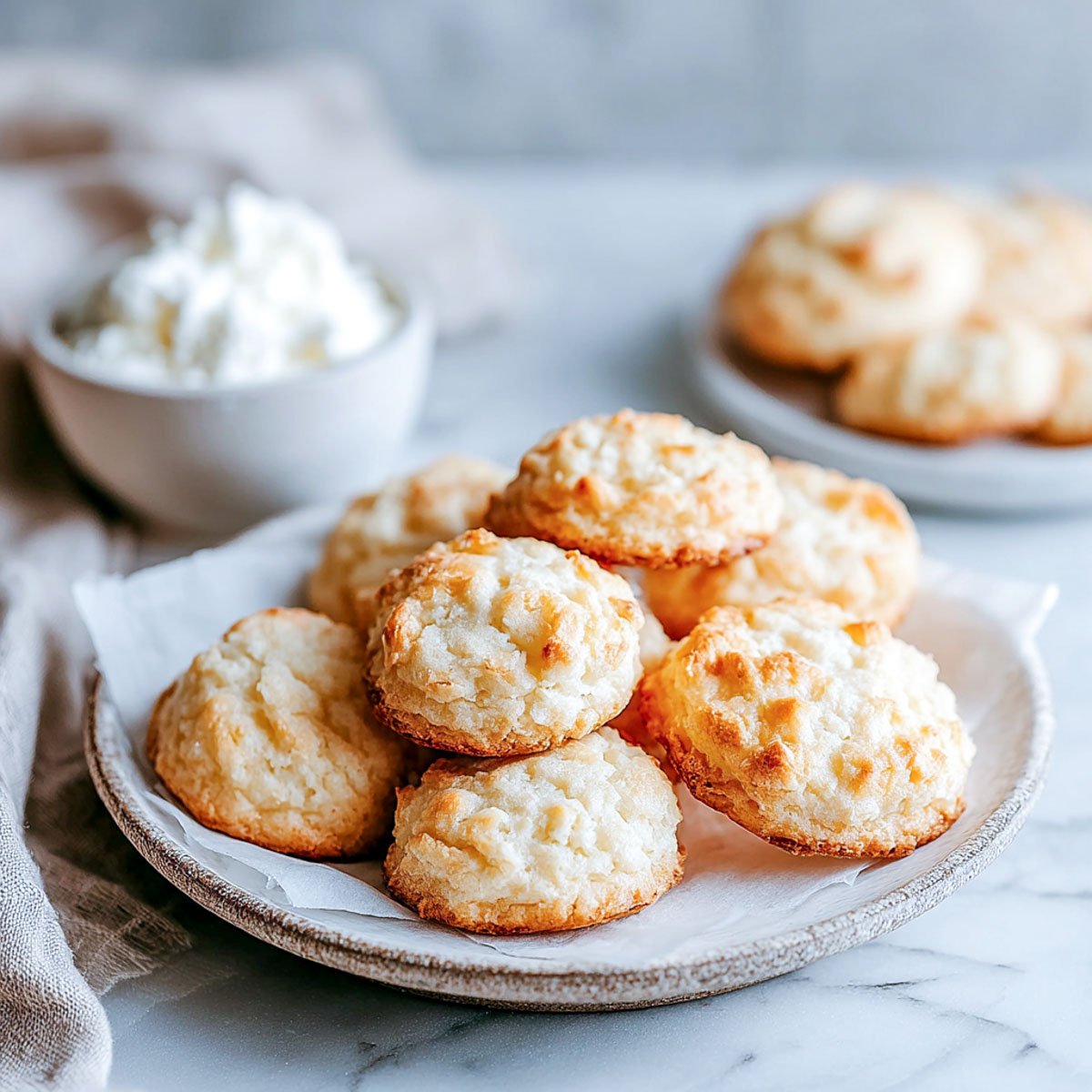 Plate of thick, golden-brown cottage cheese cookies arranged on parchment paper with a small bowl of cottage cheese and neutral linen napkin.