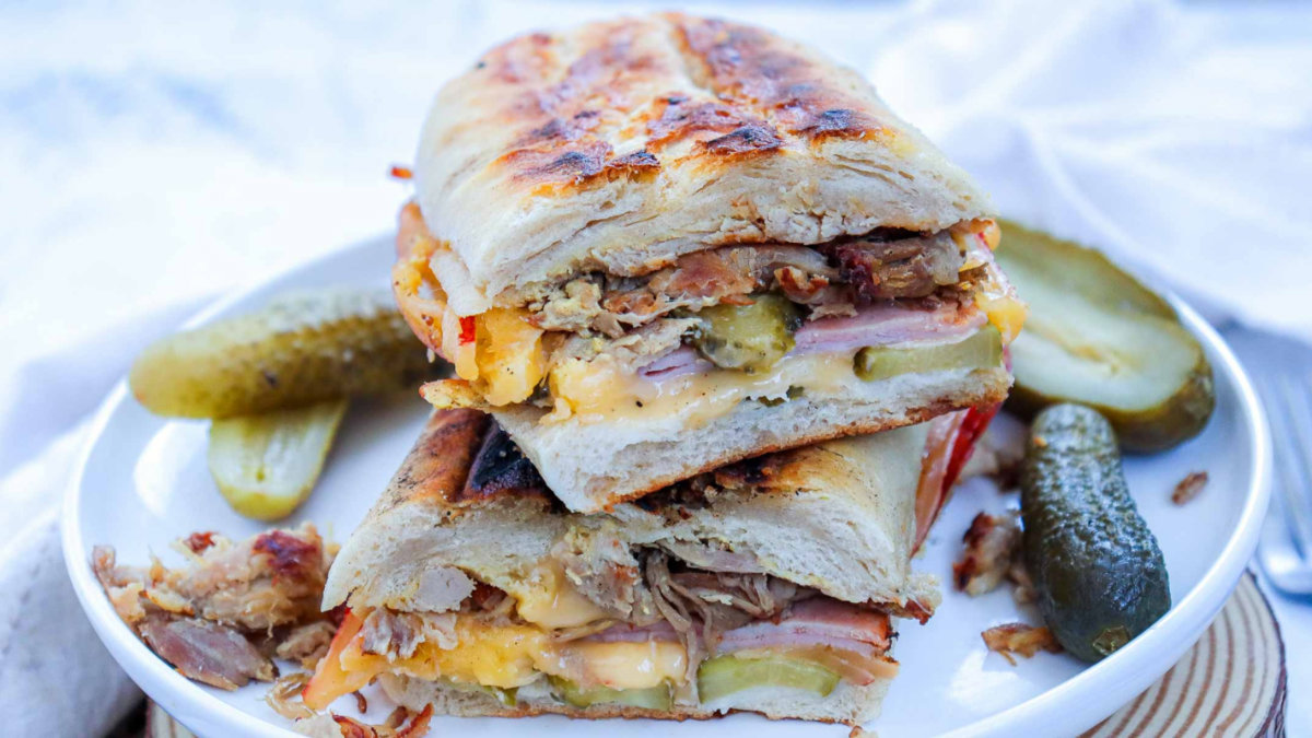 Pressed Cuban sandwich cut in half, layered with pork, ham, cheese, and pickles.