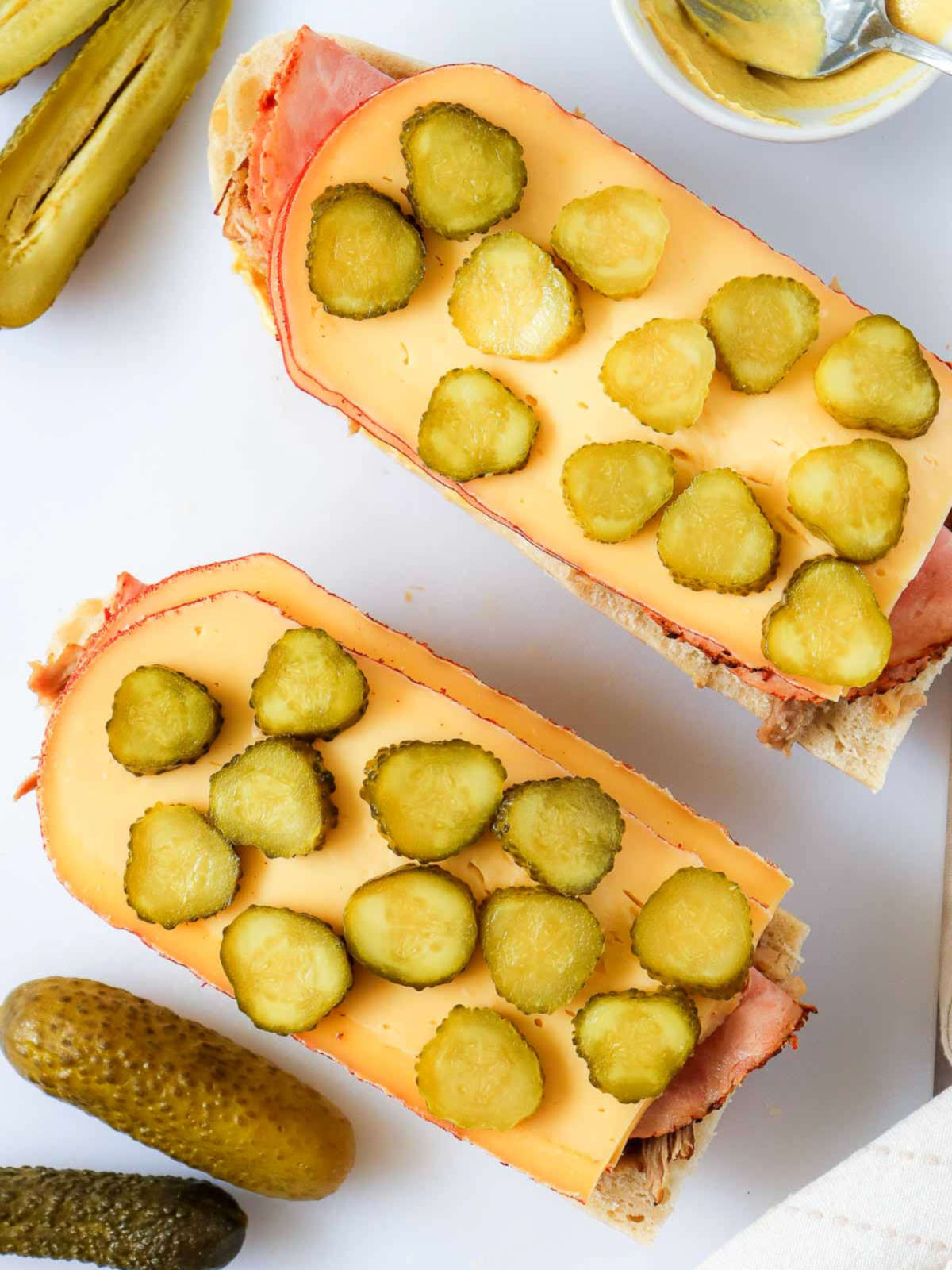 Sliced pickles and cheese layered over ham on sandwich bread.