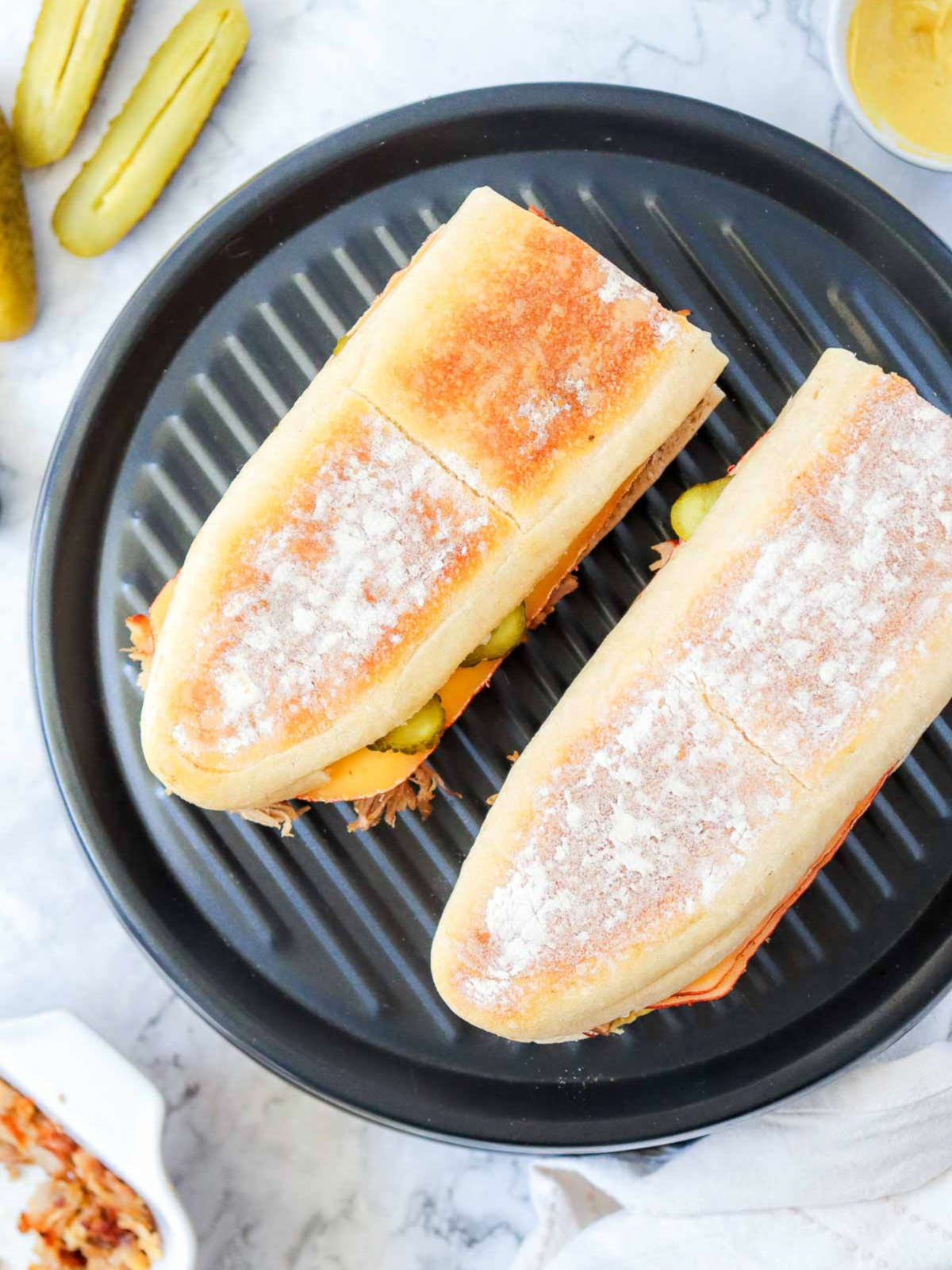 Two assembled Cuban sandwiches placed on a panini press before grilling.