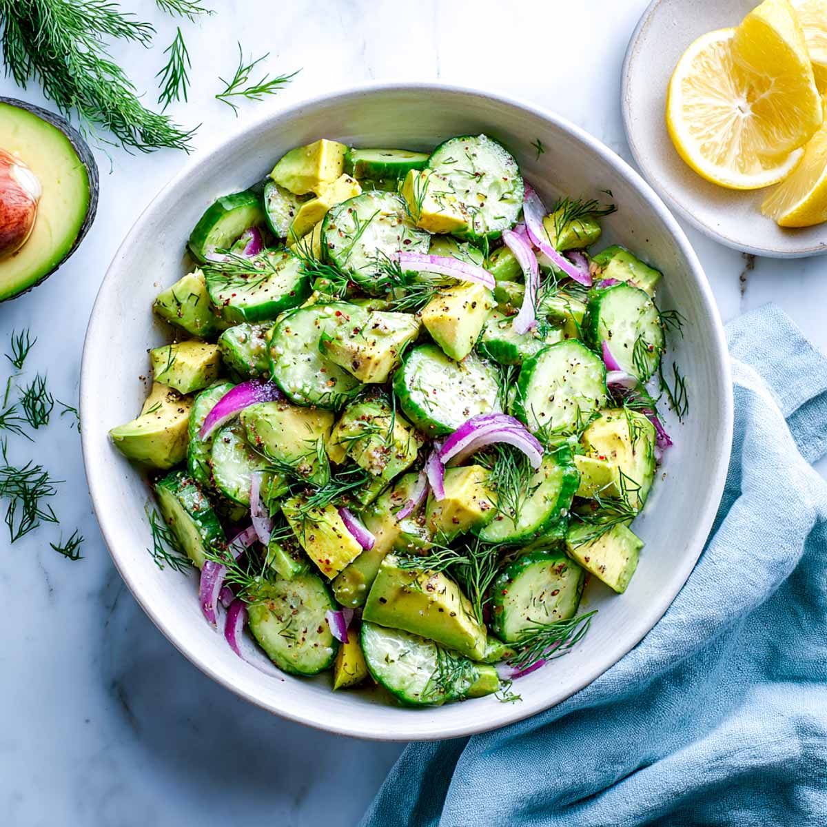 Cucumber avocado salad with red onion and fresh dill in a white ceramic bowl.