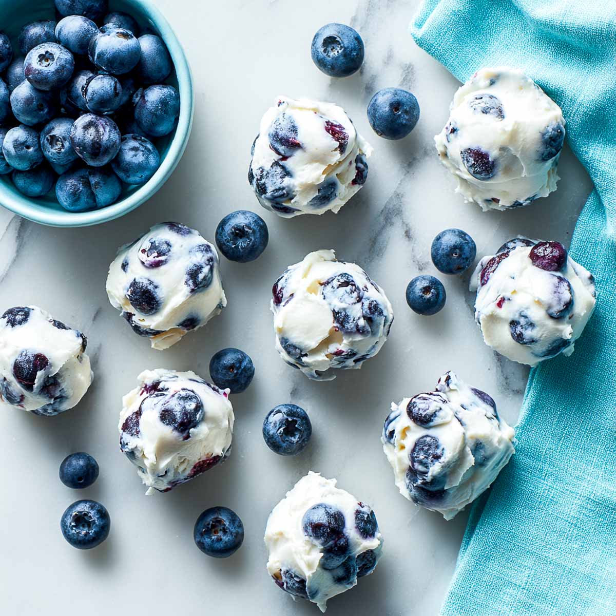 Top-down view of frozen blueberry yogurt clusters with whole berries on marble.