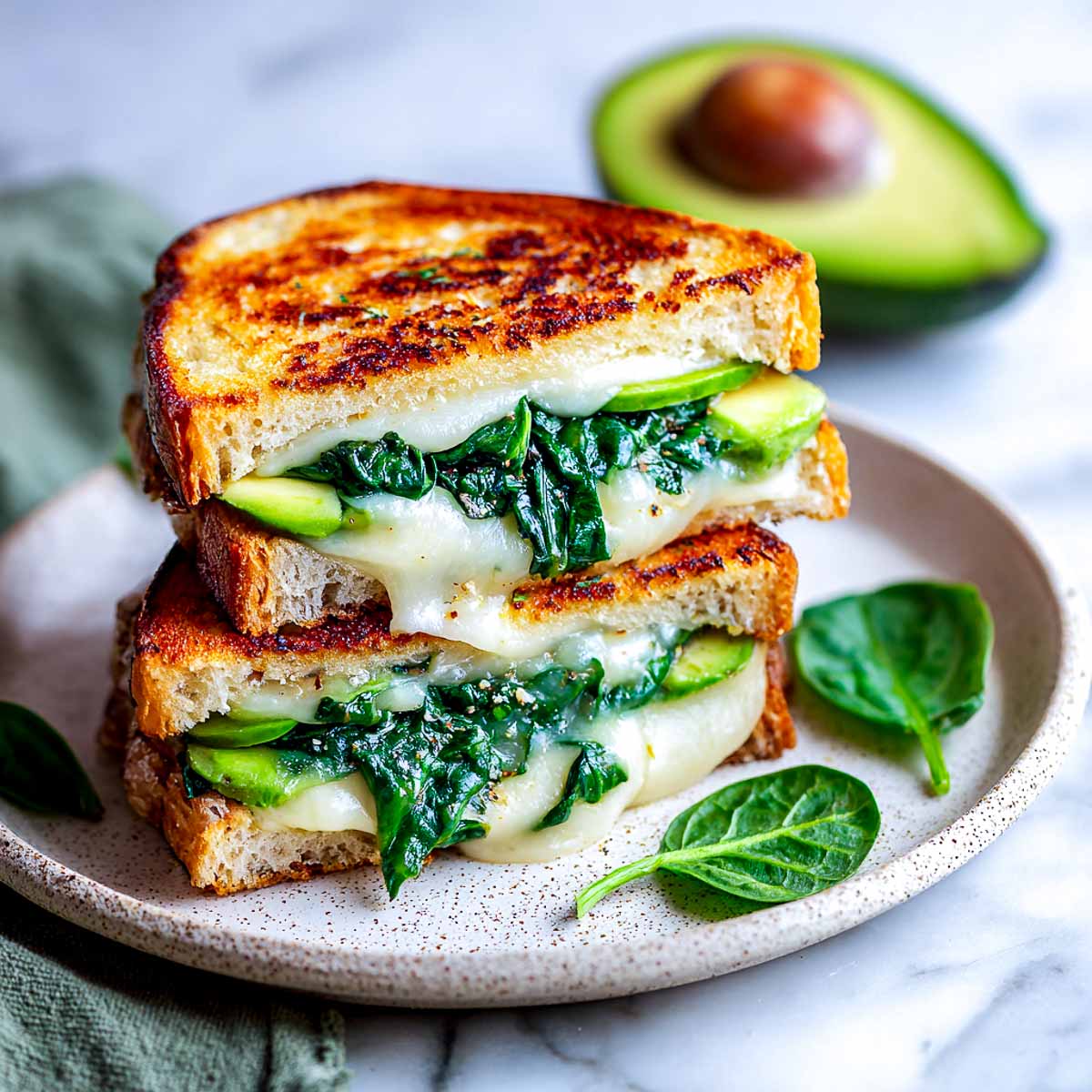 Grilled cheese sandwich with melted cheese, avocado slices, and sautéed spinach.