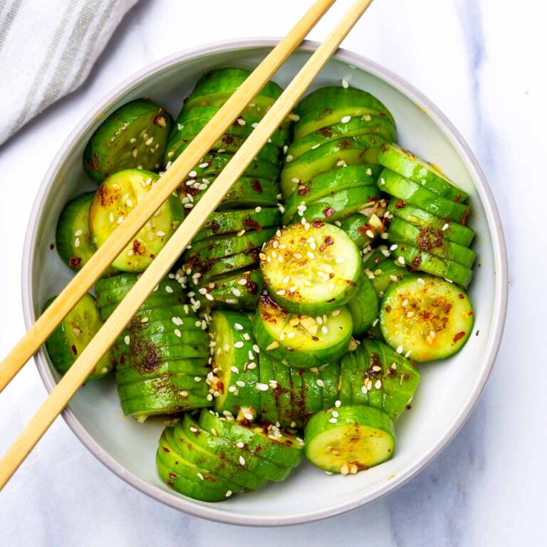 Flat lay of accordion-sliced cucumber salad with garlic chili oil, sesame seeds, and soy-based dressing, served in a bowl with chopsticks.