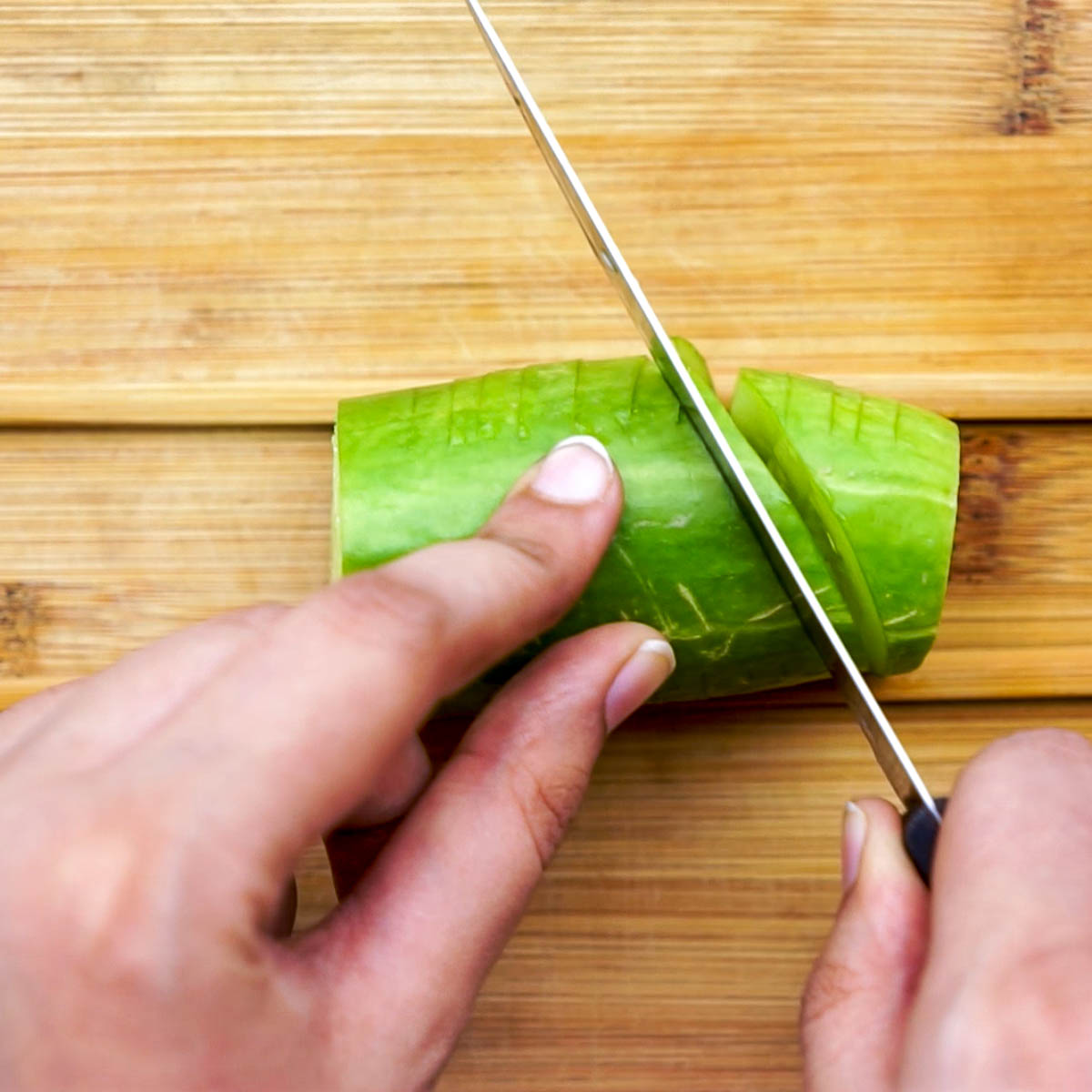 Making diagonal slices on the other side of the cucumber to create an accordion effect.