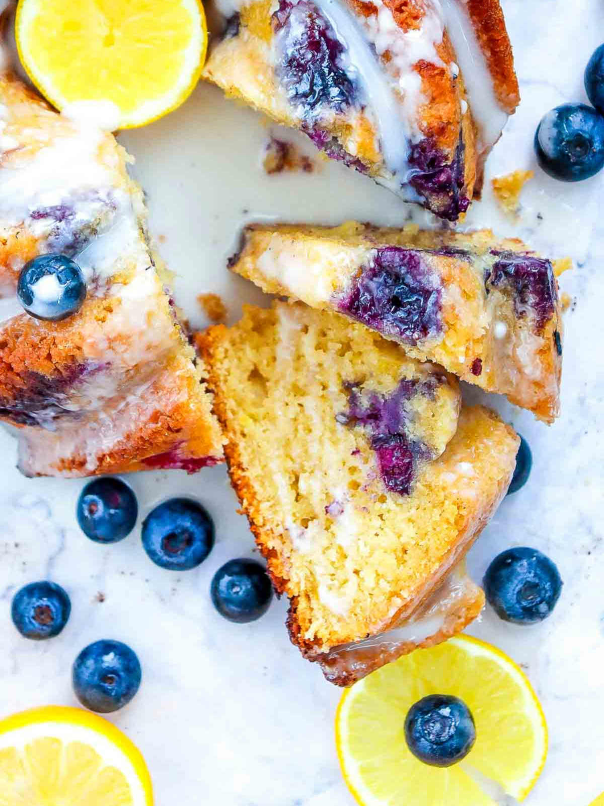 Close-up of sliced lemon blueberry bundt cake showing the soft, moist crumb and baked-in blueberries, with lemon slices and blueberries scattered around.