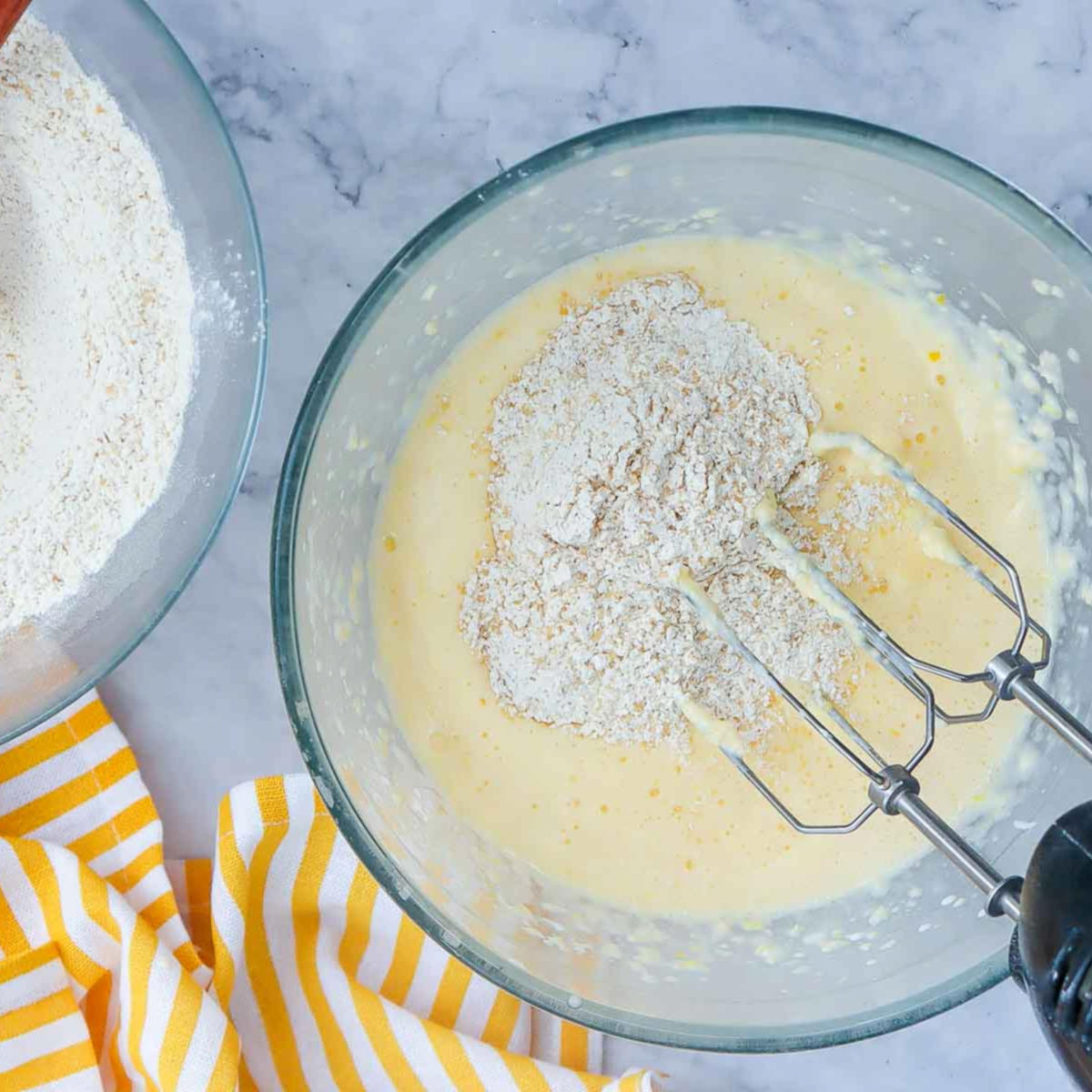 Flour mixture being added to the wet ingredients with a hand mixer, showing the batter starting to come together.