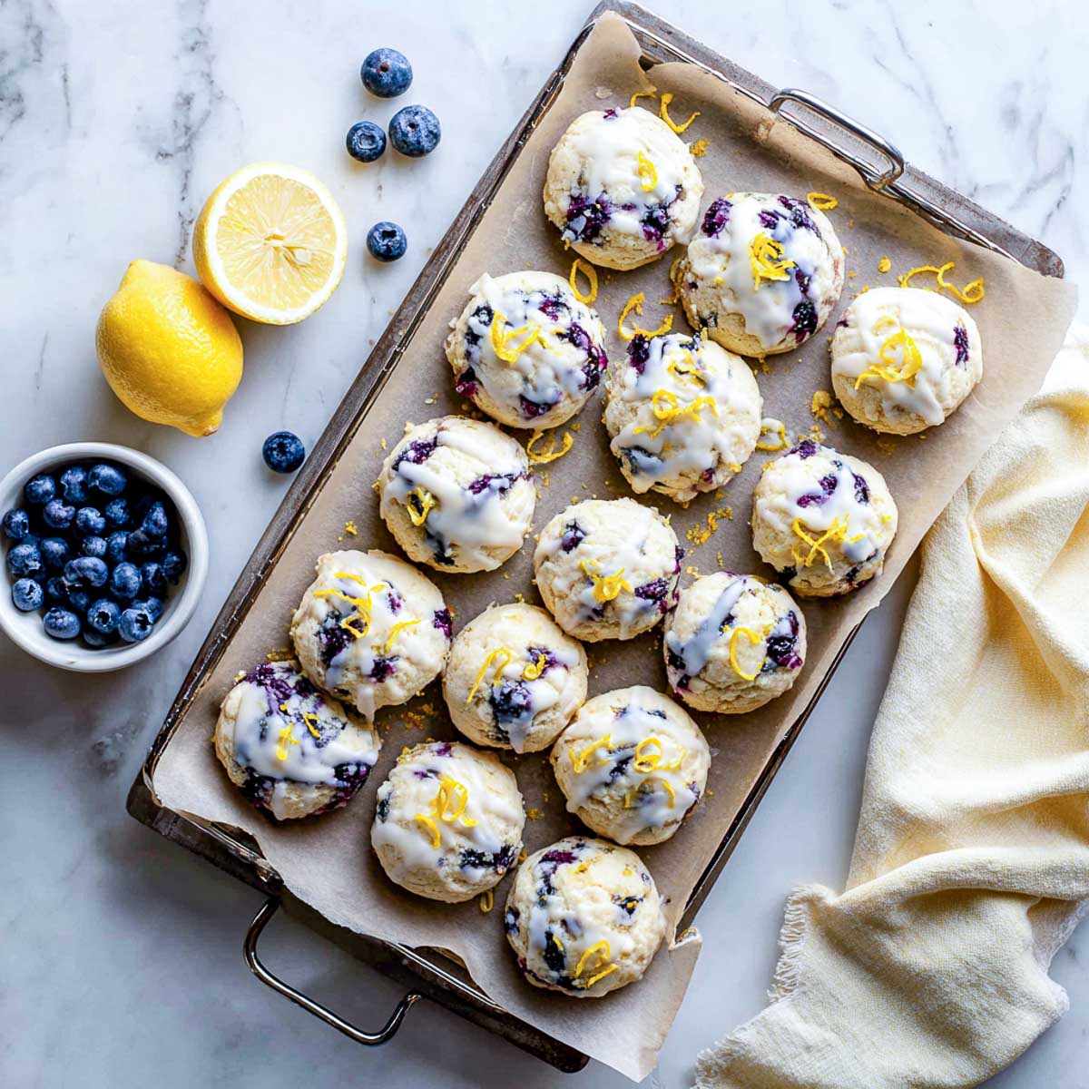 Top-down view of lemon blueberry ricotta cookies with glaze and zest on parchment.