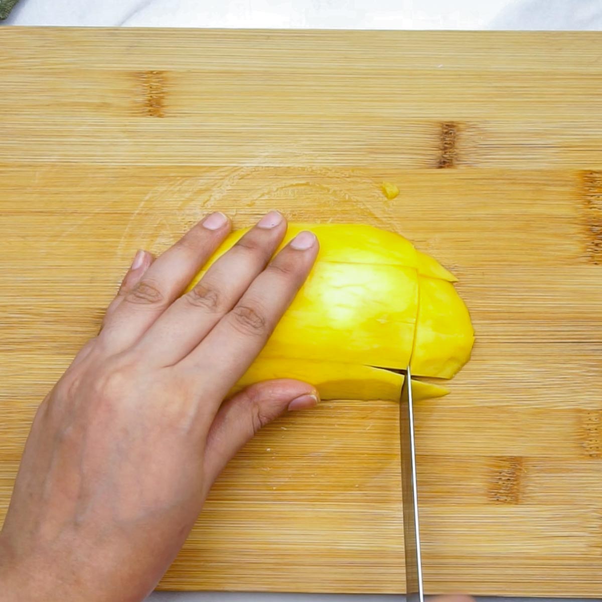 Hand slicing a peeled mango on a wooden cutting board, preparing mango chunks for lassi.