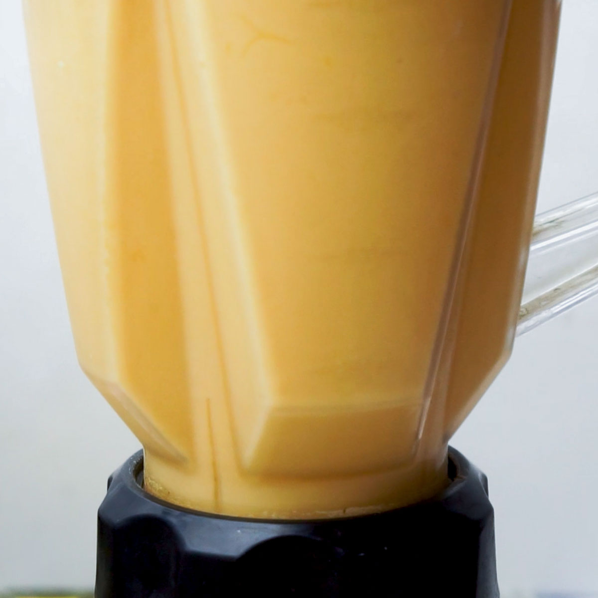 Blender jar filled with creamy mango lassi mixture in the process of blending.
