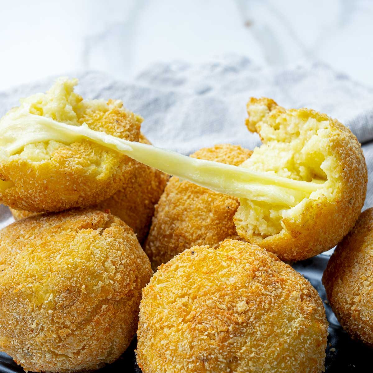 Potato cheese croquette broken open with melted cheese stretching inside.