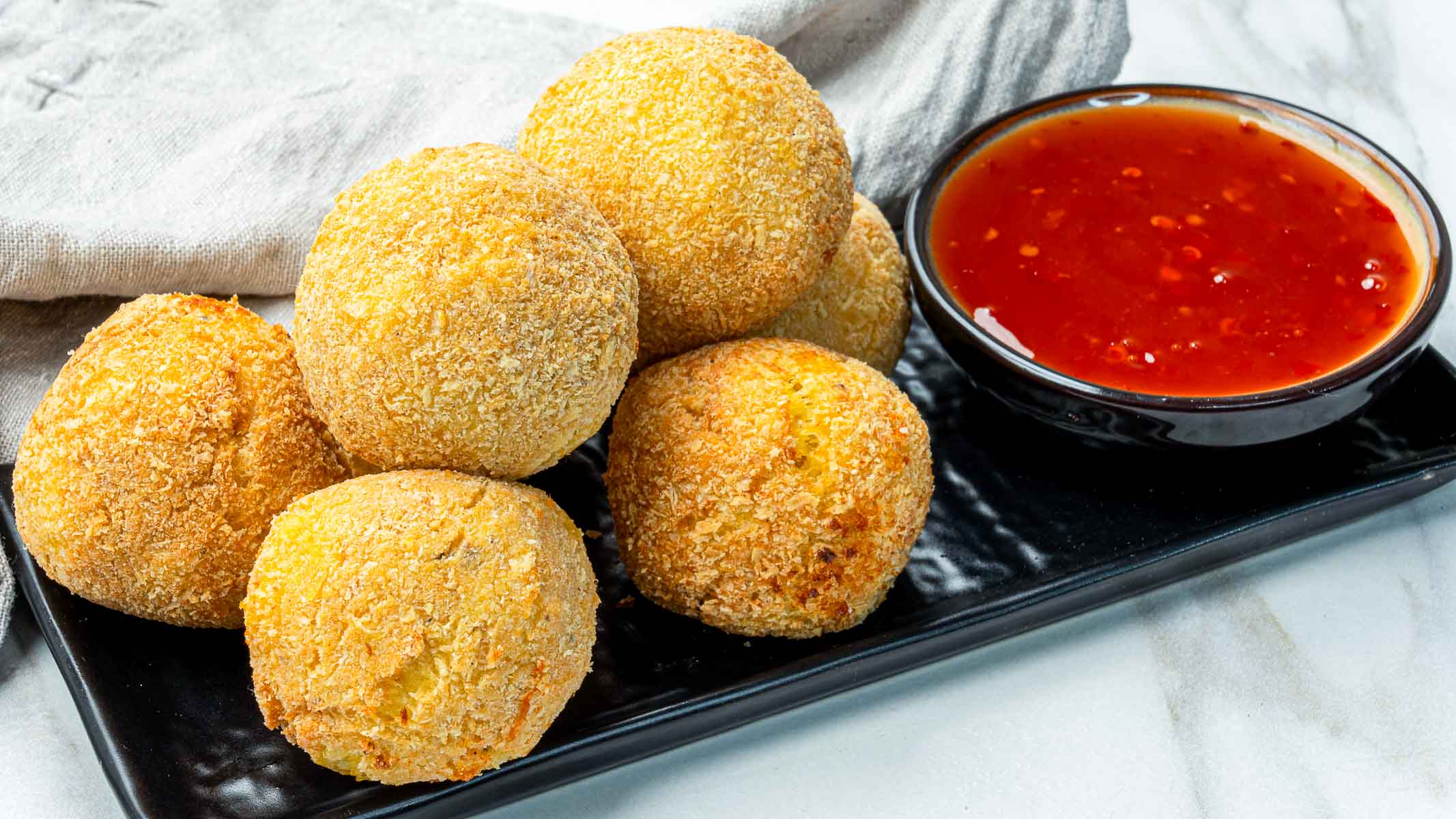 Plate of potato cheese croquettes served with a bowl of sweet chili dipping sauce.