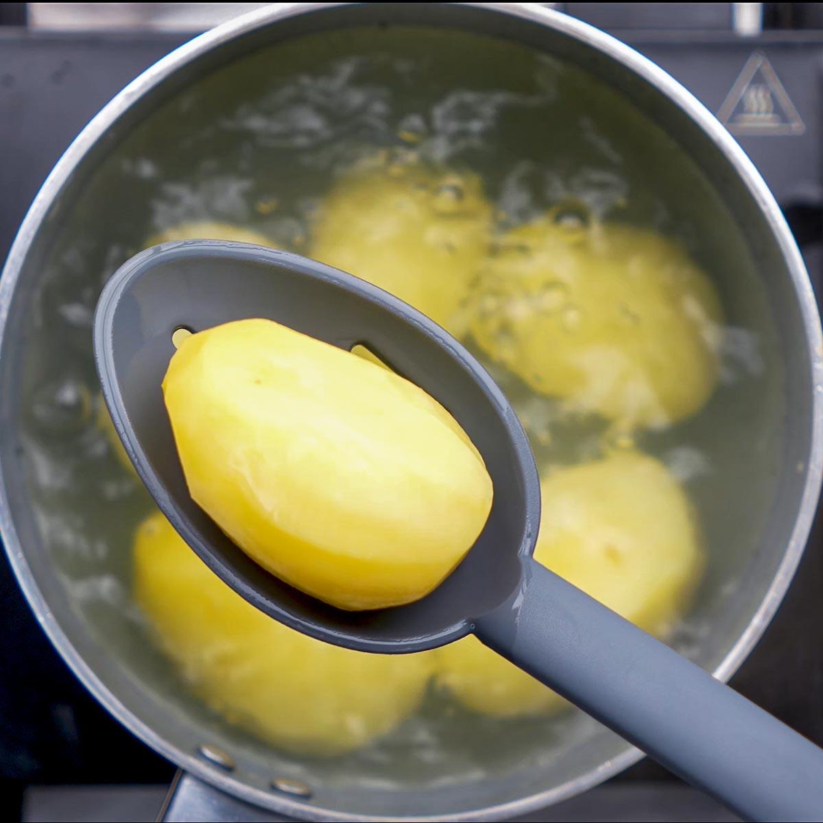 Peeled potatoes boiling in water in a stainless steel pot.