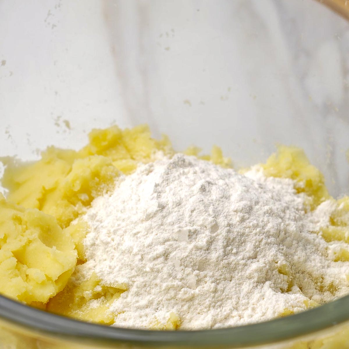 Mashed potatoes in a glass bowl with flour added on top.