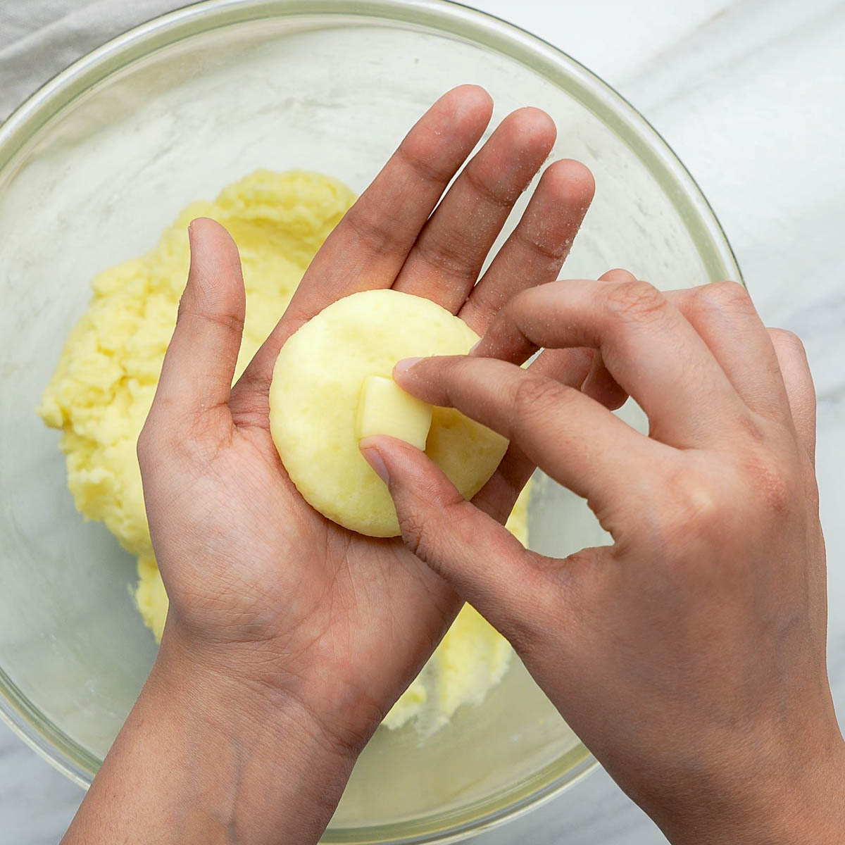 Hand placing a cube of cheese into flattened potato mixture.