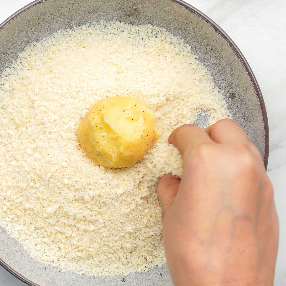 Hand rolling potato cheese ball in breadcrumbs for coating.