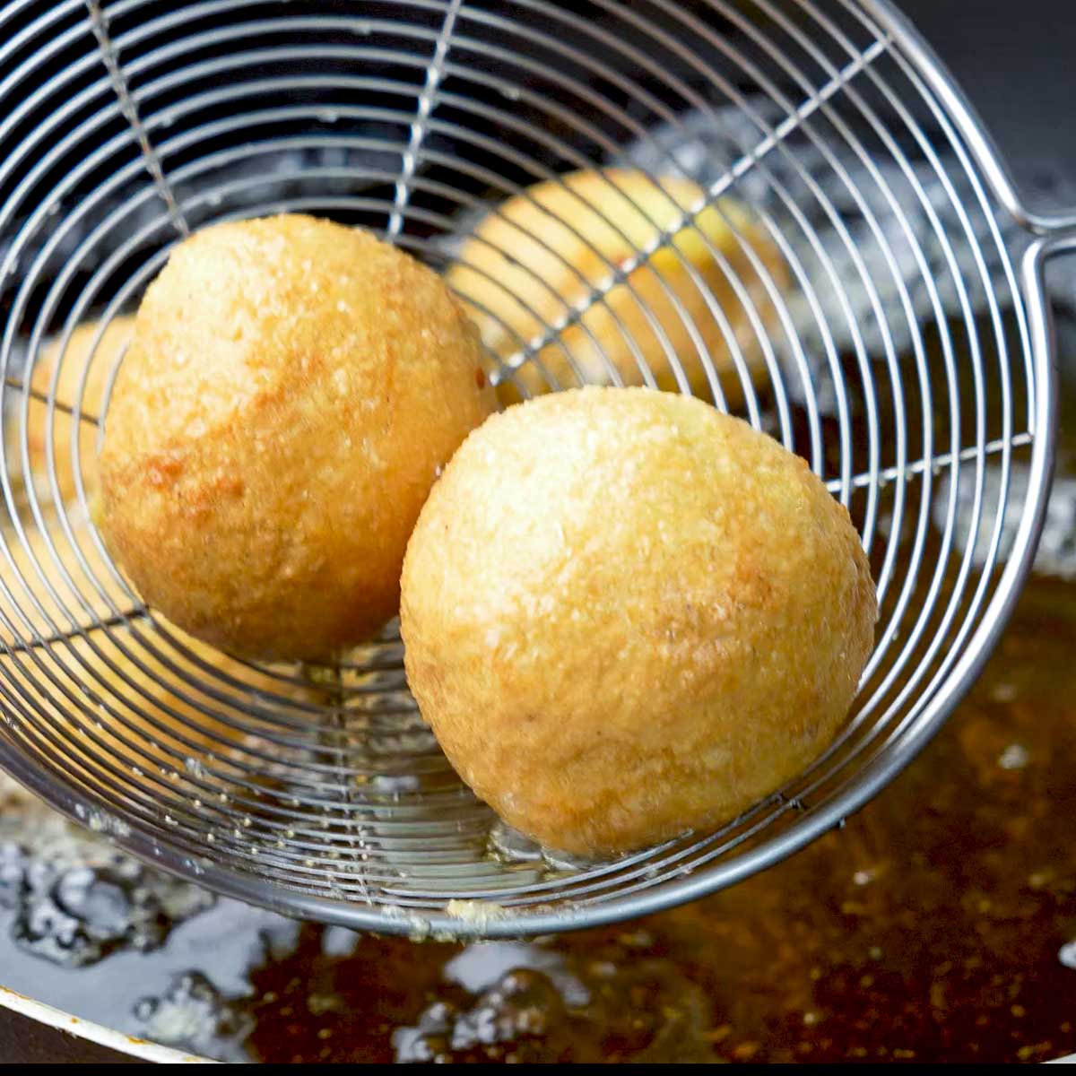 Fried potato cheese croquettes being lifted from hot oil with a strainer.