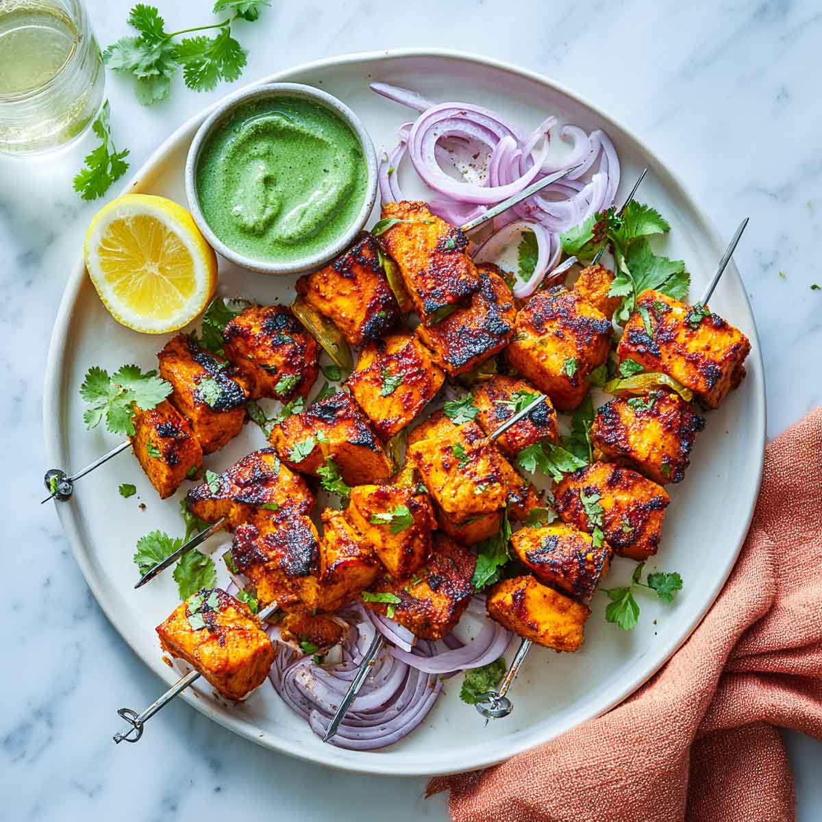 Top-down view of salmon tikka skewers with chutney, lemon, and red onions.