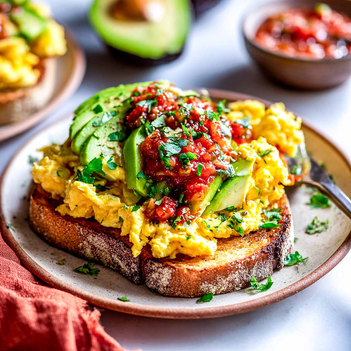 Scrambled eggs on toast with avocado slices and chunky tomato salsa on top.