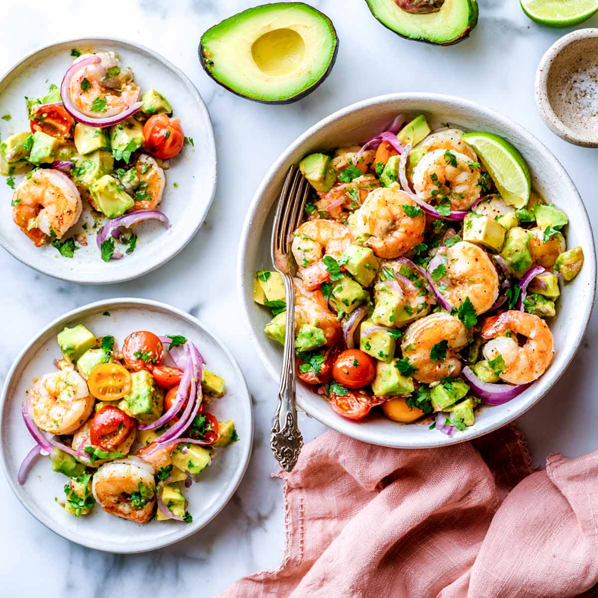 Shrimp avocado salad with cherry tomatoes and red onion on plates and in a bowl.
