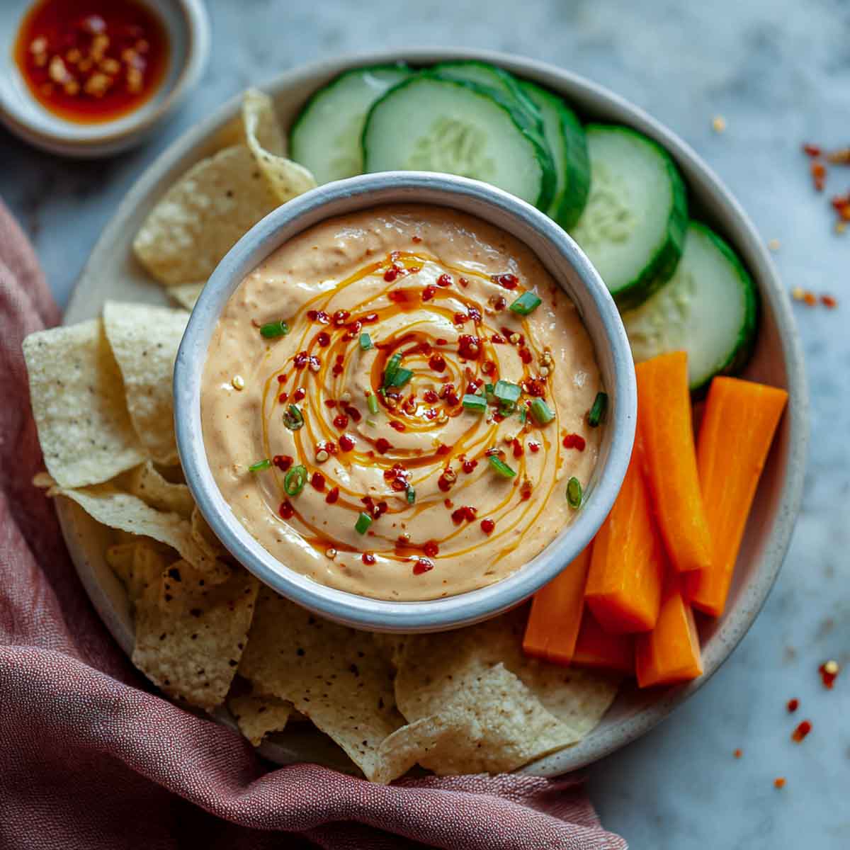 Creamy sriracha dip with chili swirl, served with chips, cucumbers, and carrots.