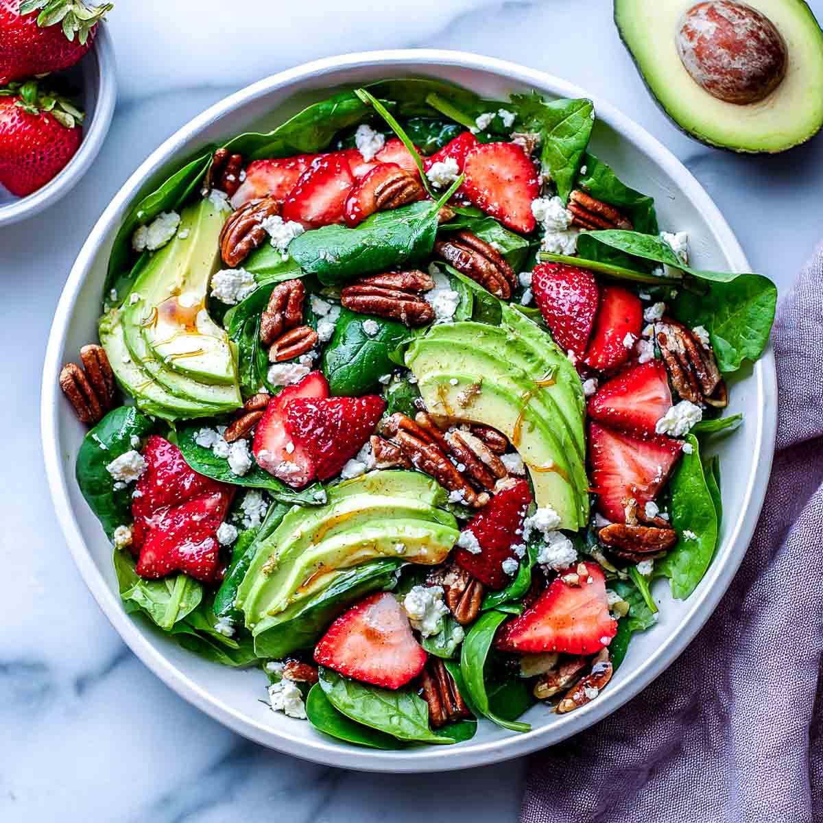 Spinach salad with strawberries, avocado slices, pecans, and crumbled feta cheese.