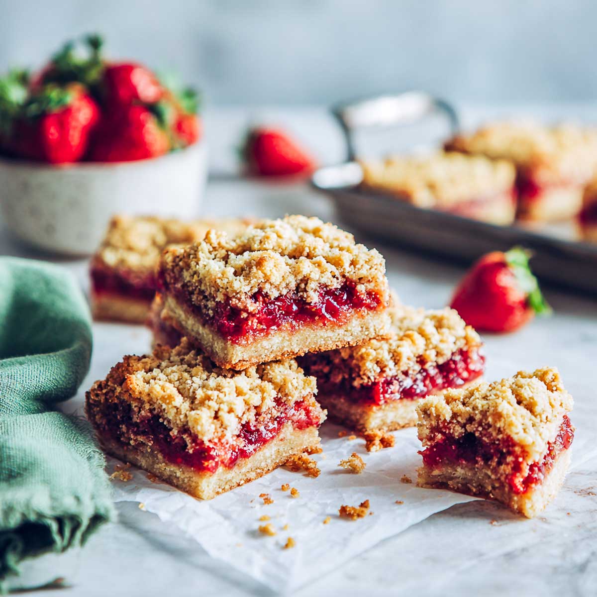 Buttery crumble bars with strawberry filling, stacked and served on parchment.