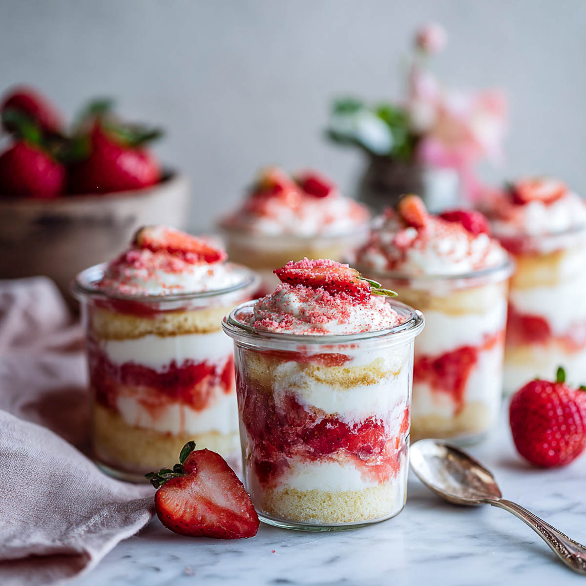 Layered strawberry tiramisu cups in glass jars with cream and crumbled topping.
