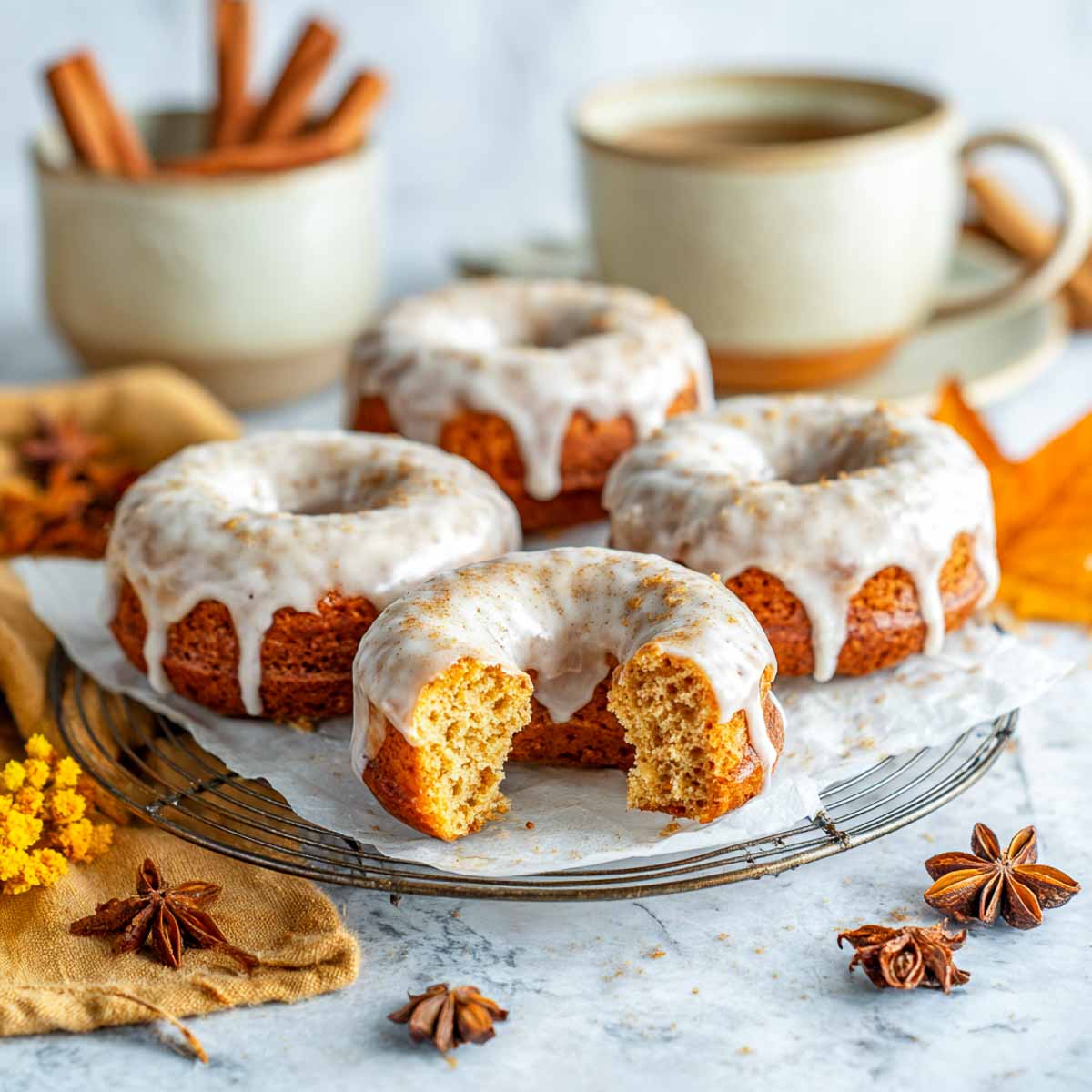 Four baked chai spiced donuts with vanilla glaze on parchment over cooling rack.