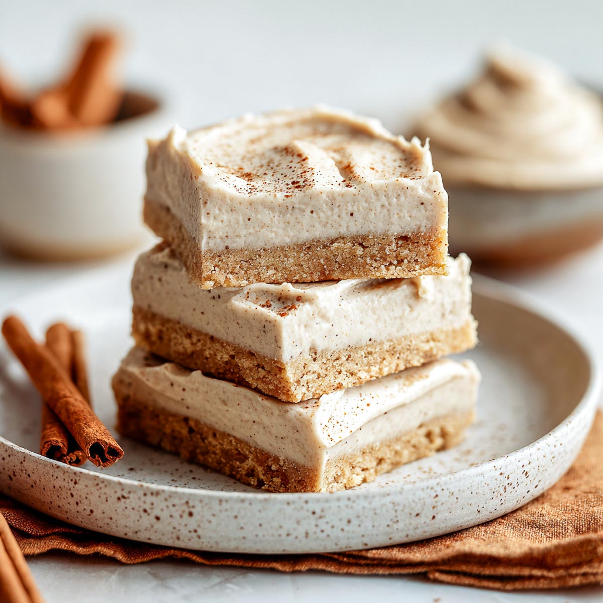 Stack of chai-spiced cookie bars with creamy frosting and cinnamon sticks in the background.