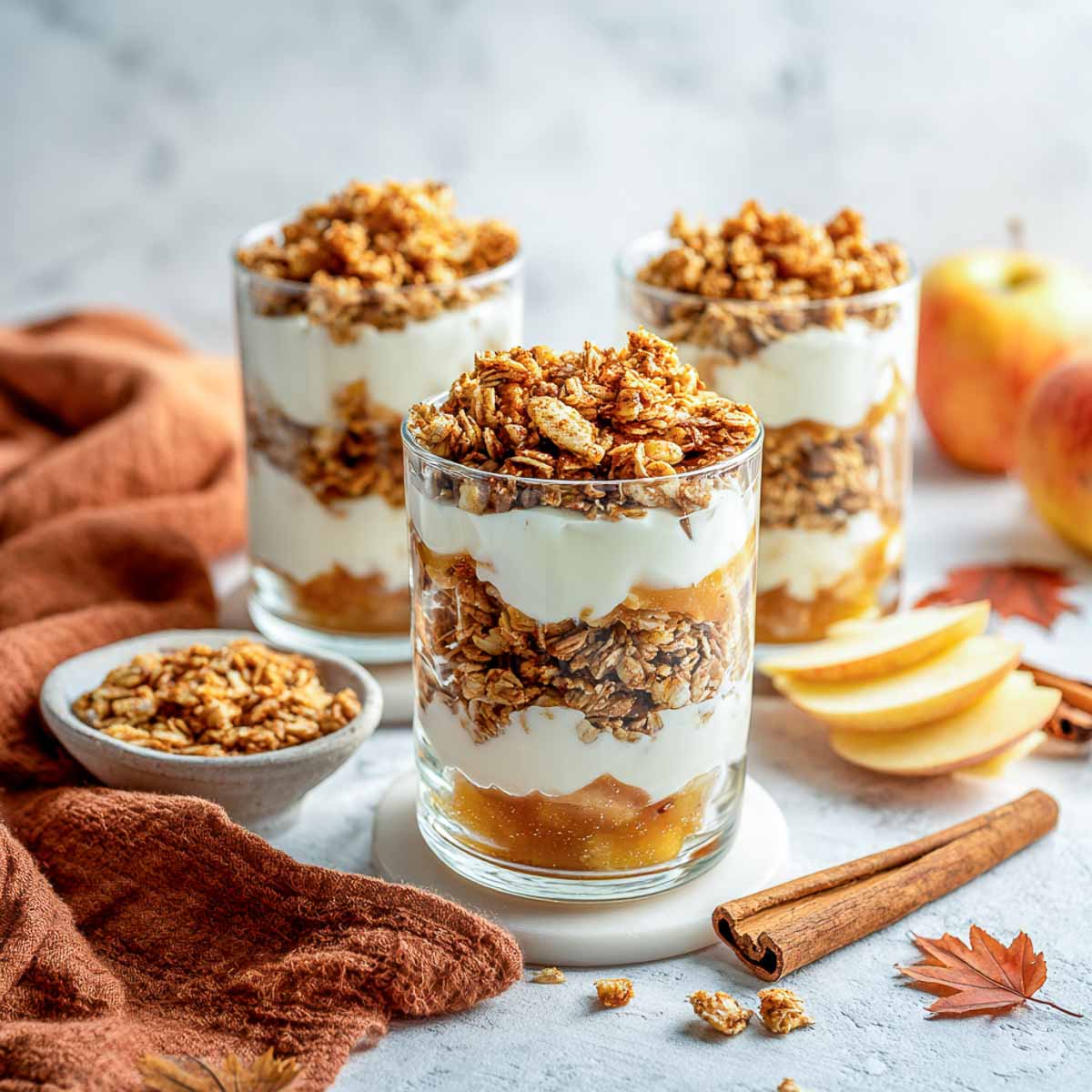 Cinnamon apple yogurt parfaits layered with granola in glass jars.