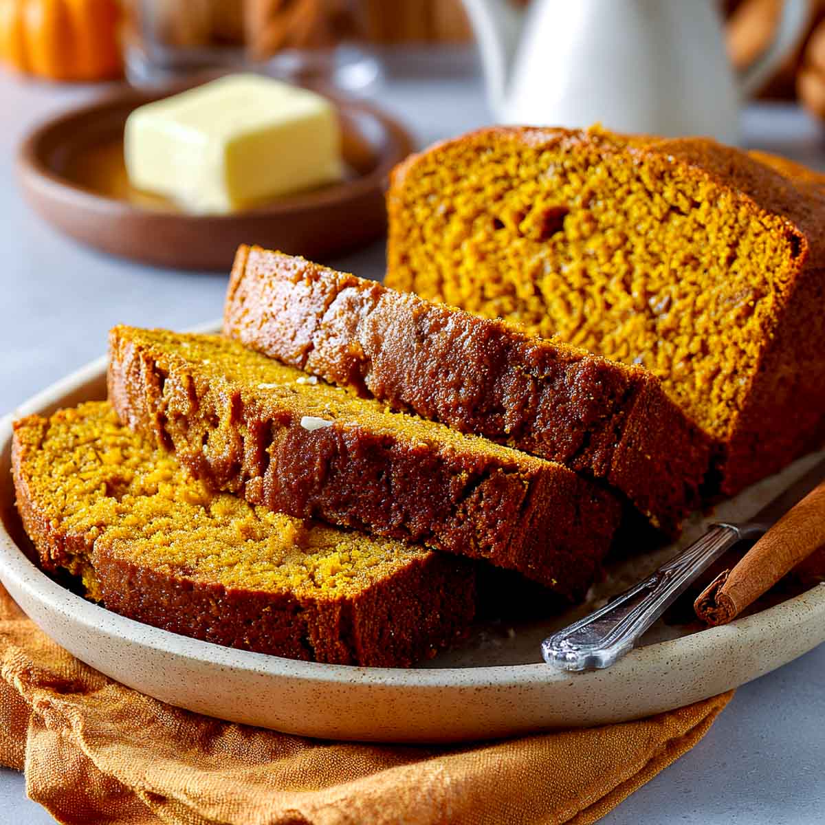 Plated slices of cottage cheese pumpkin bread with butter and cinnamon stick in the background.